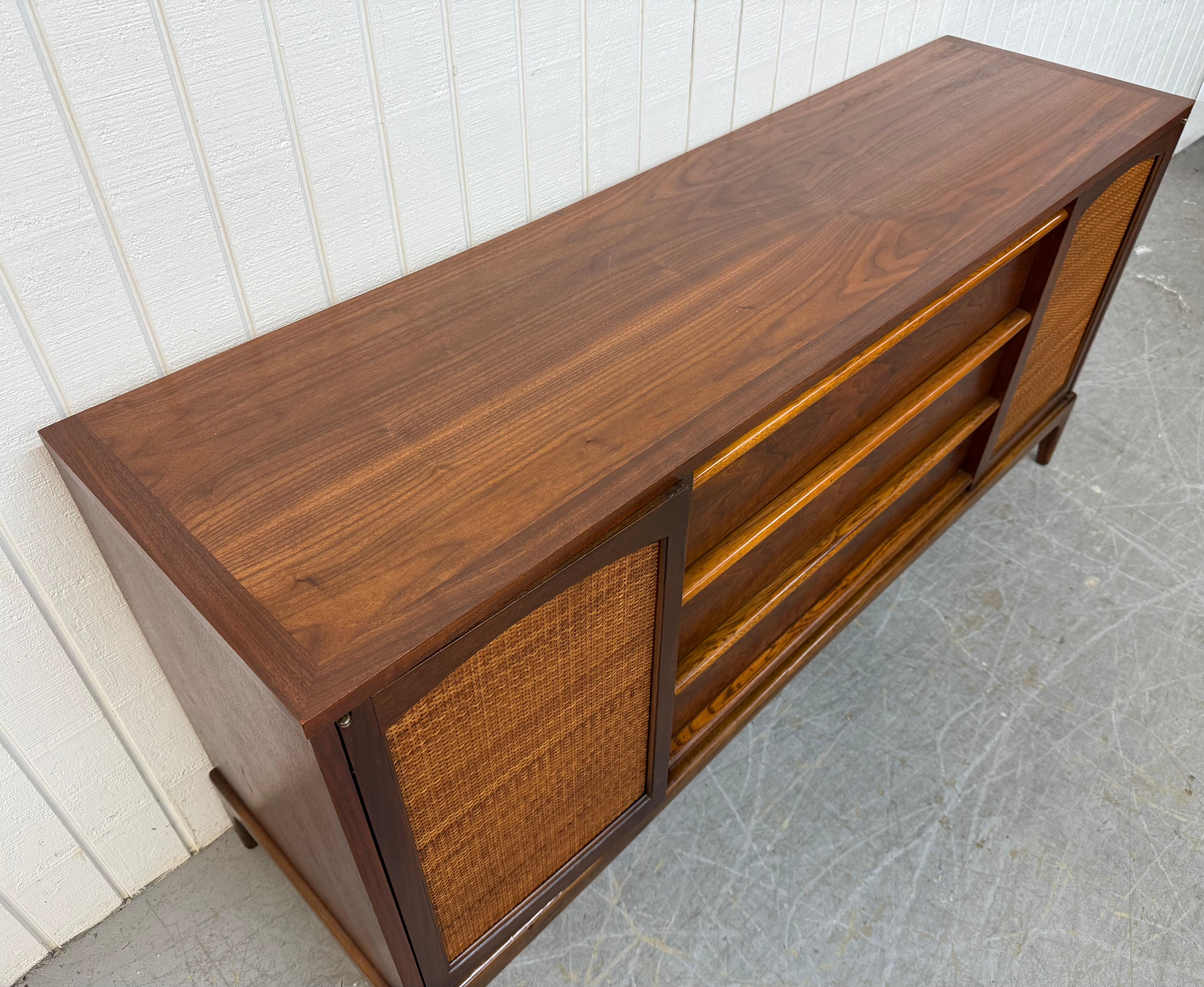 Cette annonce concerne un buffet en noyer Lane Rhythm Mid-Century Modern. Elle se caractérise par un design rectiligne, des portes en cannage à chaque extrémité qui s'ouvrent sur un espace de rangement, trois tiroirs centraux avec des poignées en
