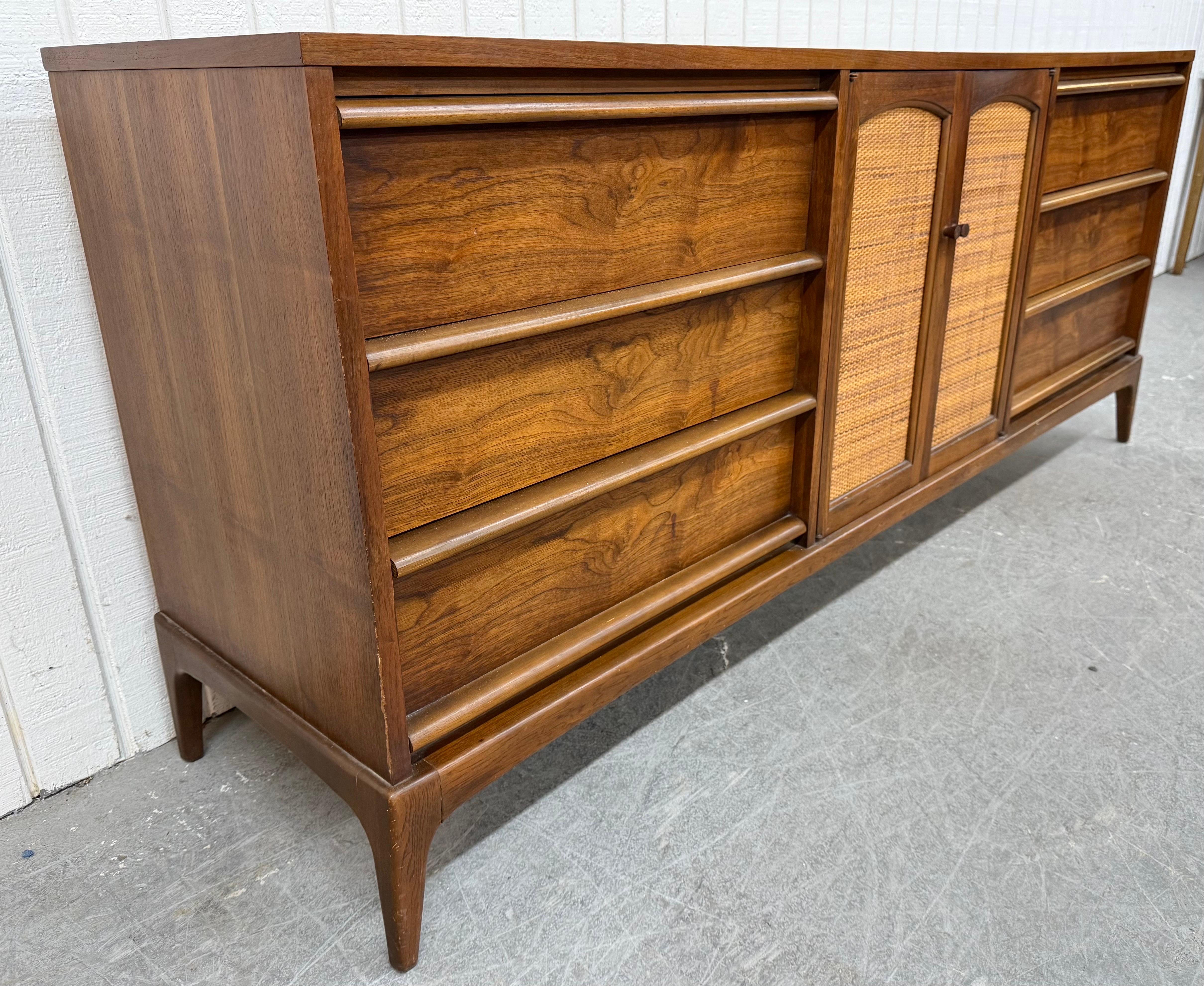 The listing is for a Mid-Century Modern Lane Rhythm Walnut Dresser. Featuring a straight line design, three drawers on each side with wooden pulls, cane center doors that open up to three hidden drawers, modern legs, and a beautiful walnut finish.