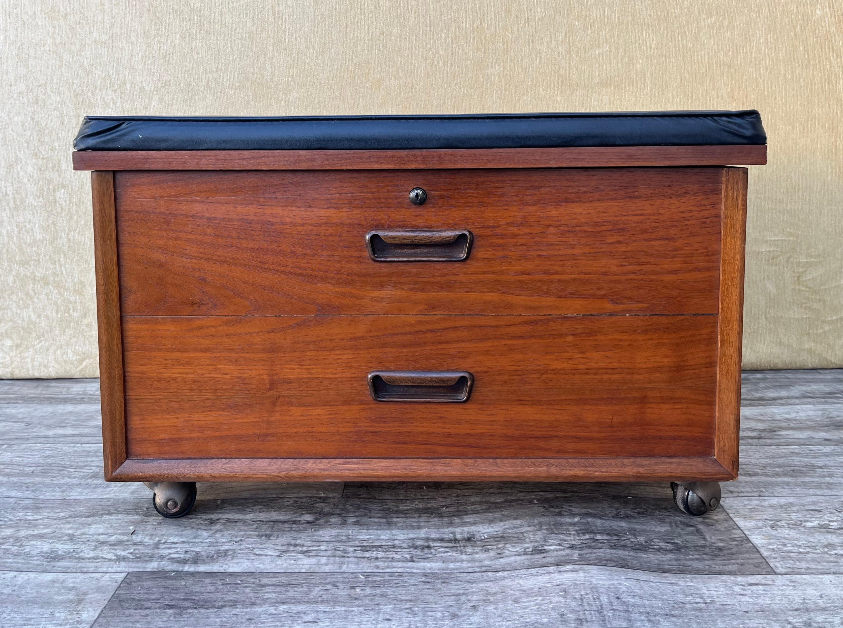 Vintage Mid Century Modern Lane Rolling Record Storage Bench. Circa 1970s. 
Features a beautiful walnut wood grain, two from faux drawers, the original black vinyl upholstery, and casters for easy mobility.
In good original condition with signs of