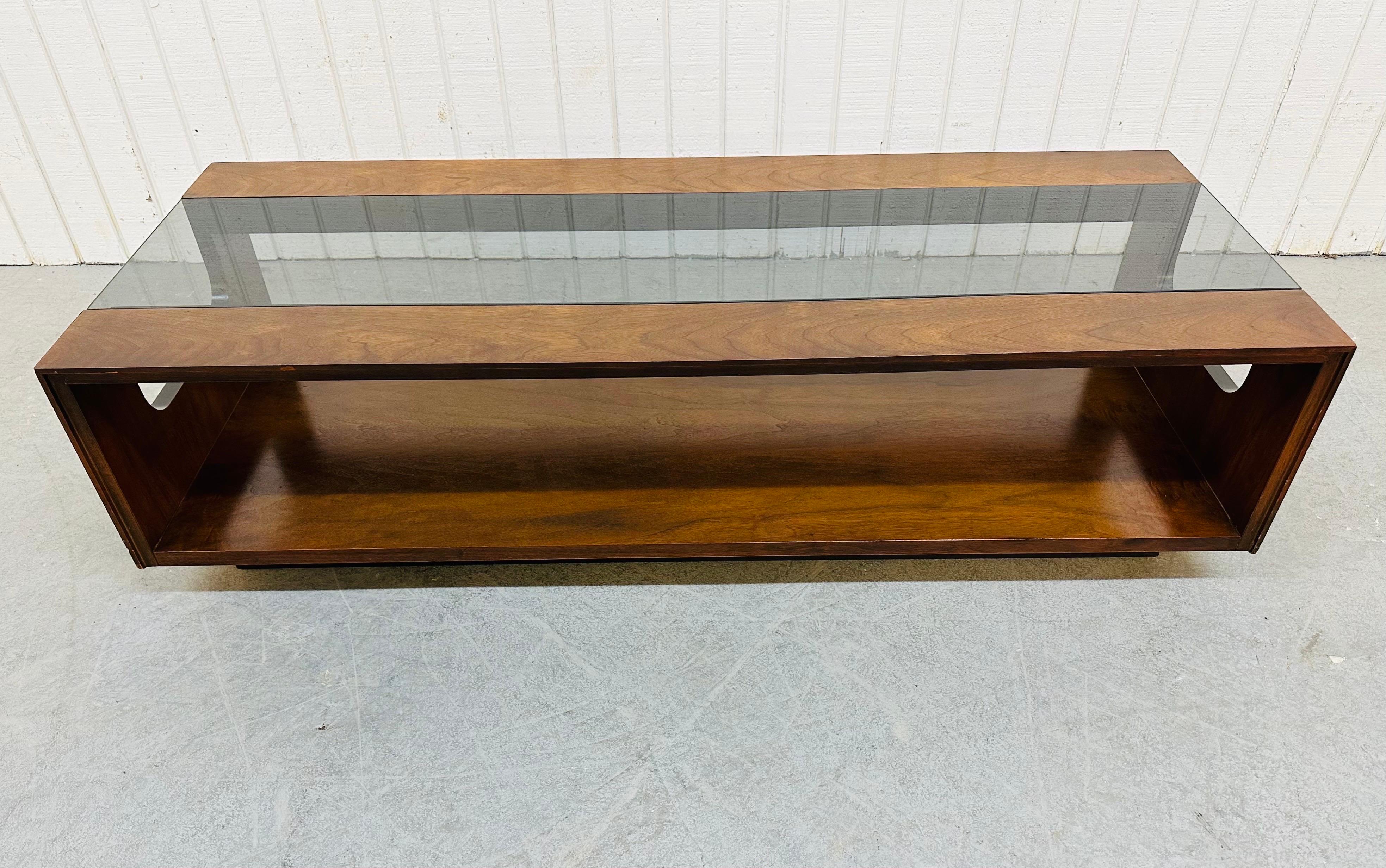 This listing is for a Mid-Century Modern Lane Walnut Smoked Glass Coffee Table. Featuring a straight line design, rectangular top with smoked glass insert, bottom tier for storage space, black plinth base, and a beautiful walnut finish. This is an