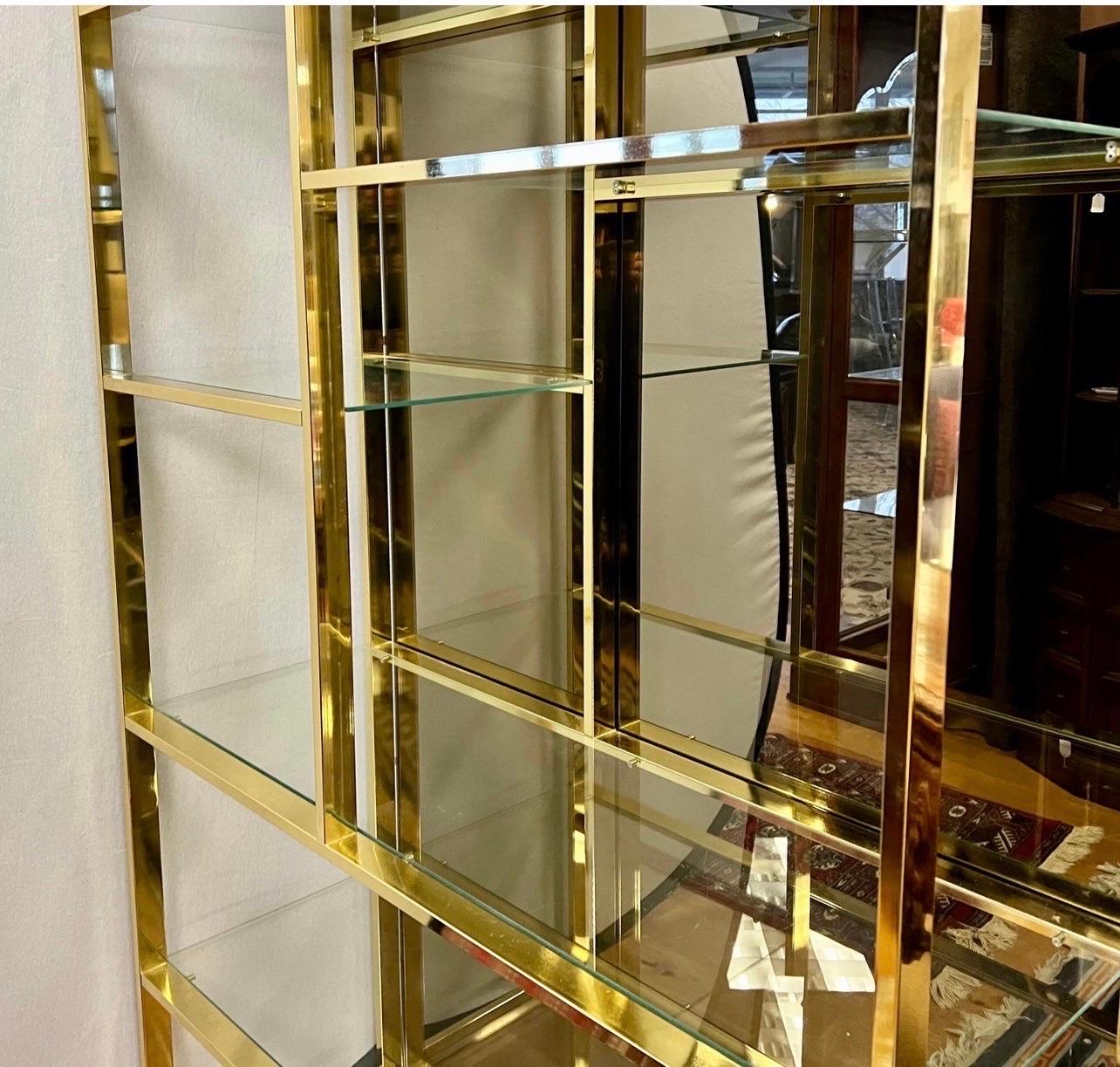 Magnificent mid-century brass and glass display etagere vitrine with mirrored back. Features two lights that illuminate from above. The geometric, staggered shelving allows optimal space to display books, picture frames, collectibles and much more.