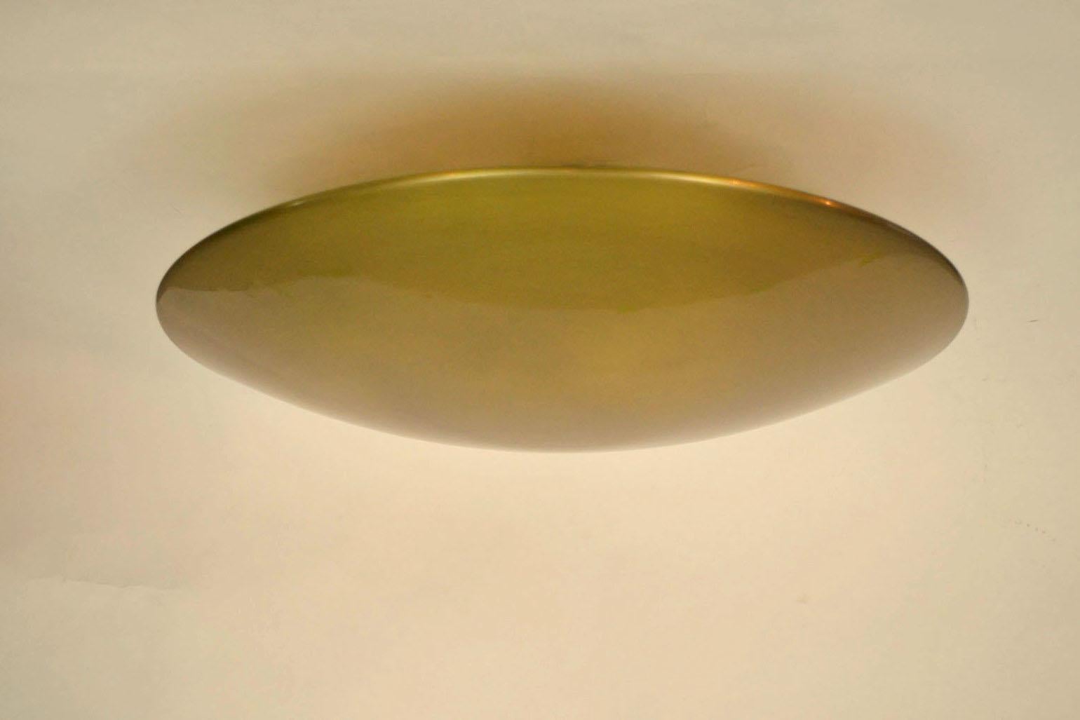 Large curved circular brass flush mount ceiling or wall lamp reflecting its surrounding like a fish eye mirror. The light radiates indirect from five light bulbs positioned around the stem under the shade to give indirect light. The dish is spun out