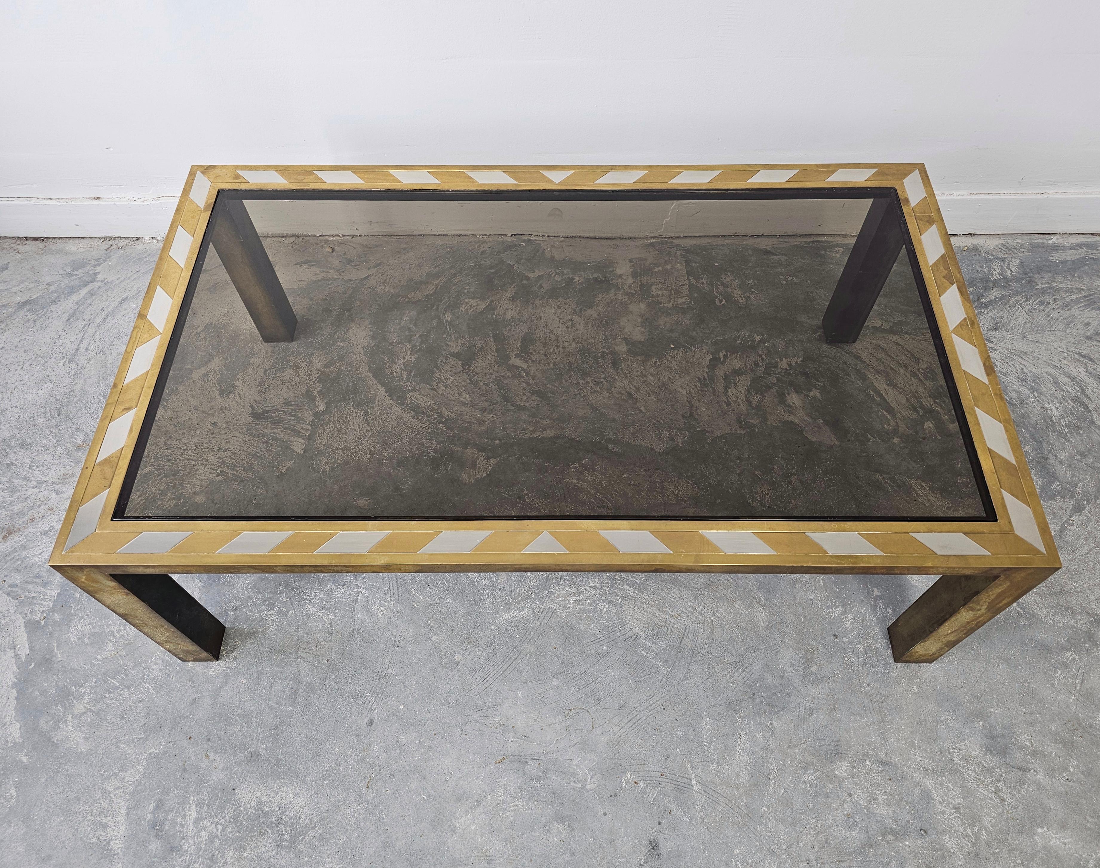 In diesem Angebot finden Sie einen spektakulären Mid Century Modern Couch- oder Sofatisch aus Messing mit vernickelten Intarsien. Tisch mit Platte aus Rauchglas. Der Tisch ist äußerst attraktiv und im Stil von Romeo Rega gestaltet, der in seinen