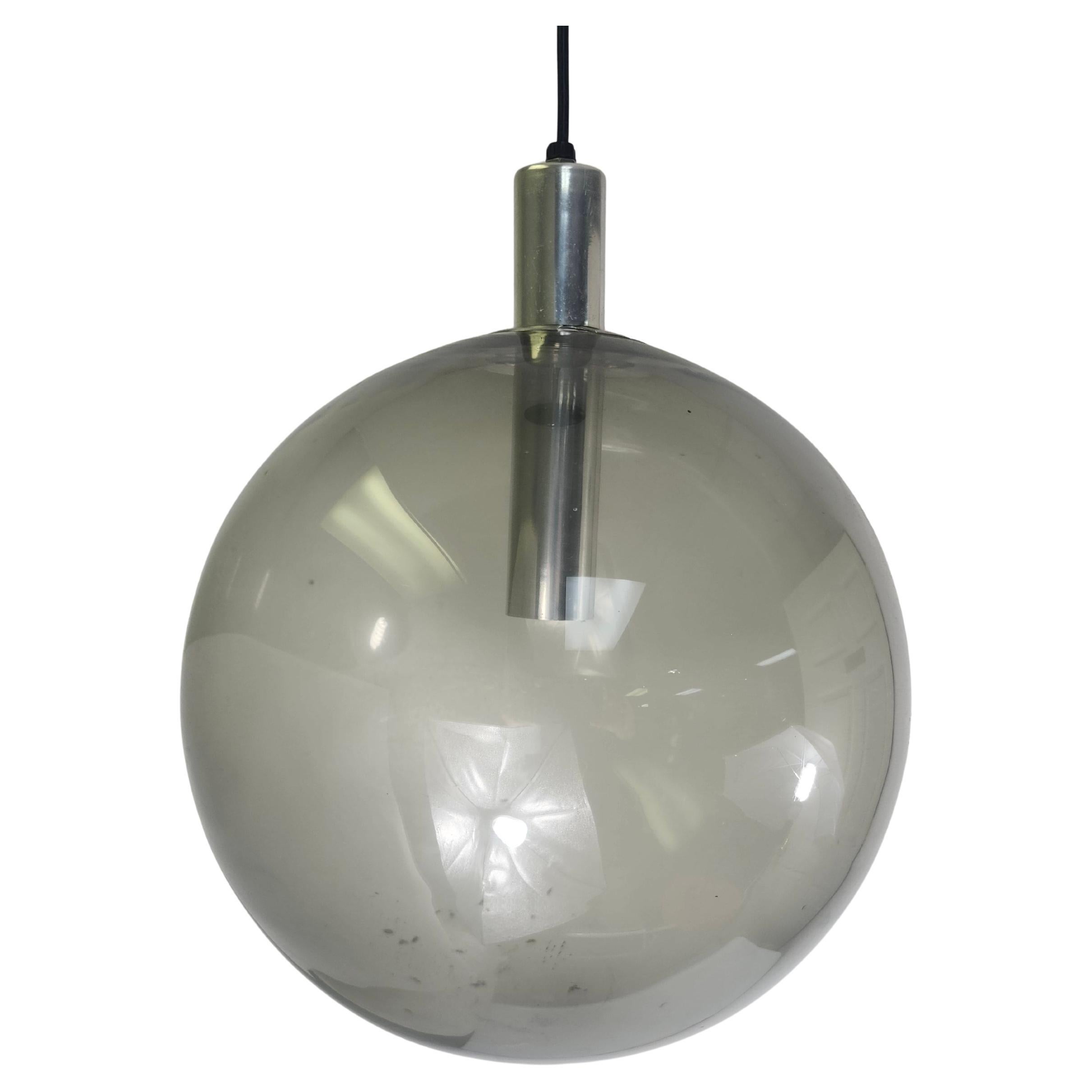 Diseño sencillo y elegante con un gran orbe de cristal ahumado y la bombilla como punto focal con el casquillo encapsulado en acero inoxidable, suspendido por un cordón pero realmente sostenido por la brida de acero inoxidable que se asienta en la