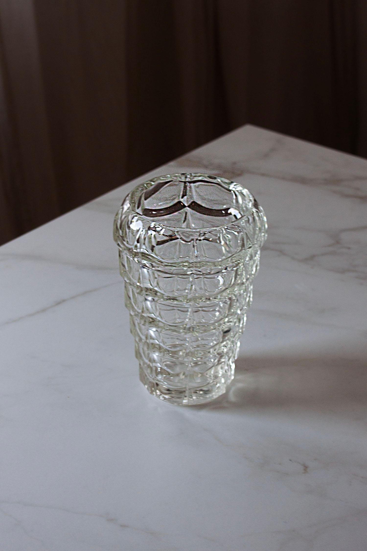 Questo vaso di grande effetto è realizzato in cristallo trasparente tagliato a mano e presenta un audace disegno geometrico di strati sfaccettati impilati che catturano e rifrangono magnificamente la luce. La sua forma scultorea lo rende tanto un