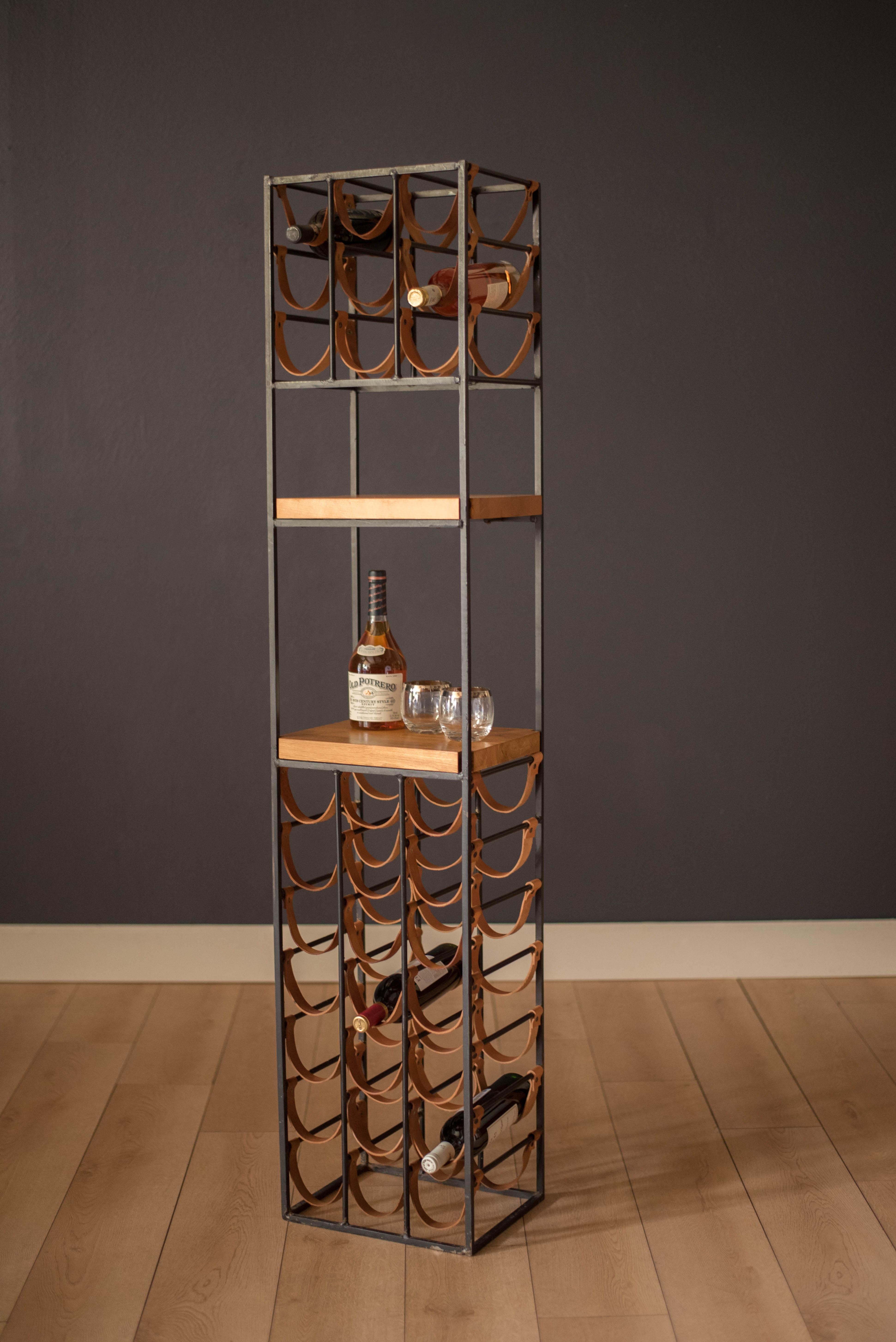 Vintage tall wine rack designed by Arthur Umanoff for Shaver Howard, circa 1950s. This piece is constructed of heavy cast black iron and tan leather saddle straps that hold up to 30 bottles. Features two butcher block shelves for cocktail serving or