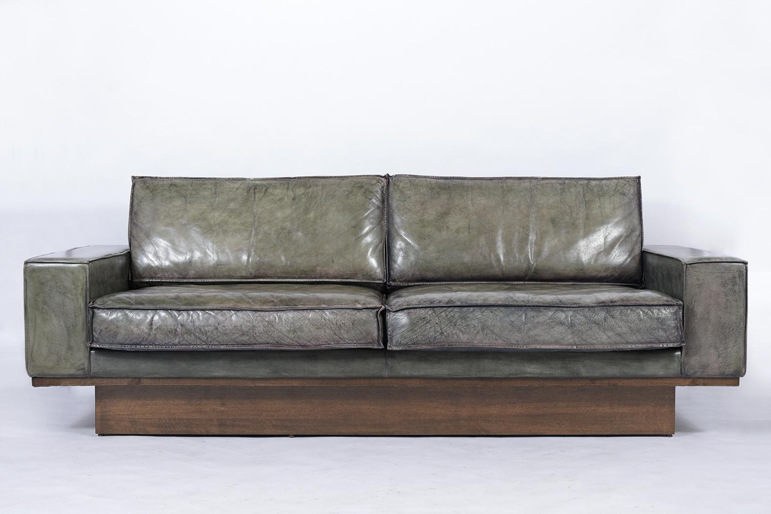 This mid-century modern sofa is upholstered in its original leather, which has been professionally dyed green with blue undertones and is in great condition. The sofa has single piping details, and comfortable foam and feather inserts. This large