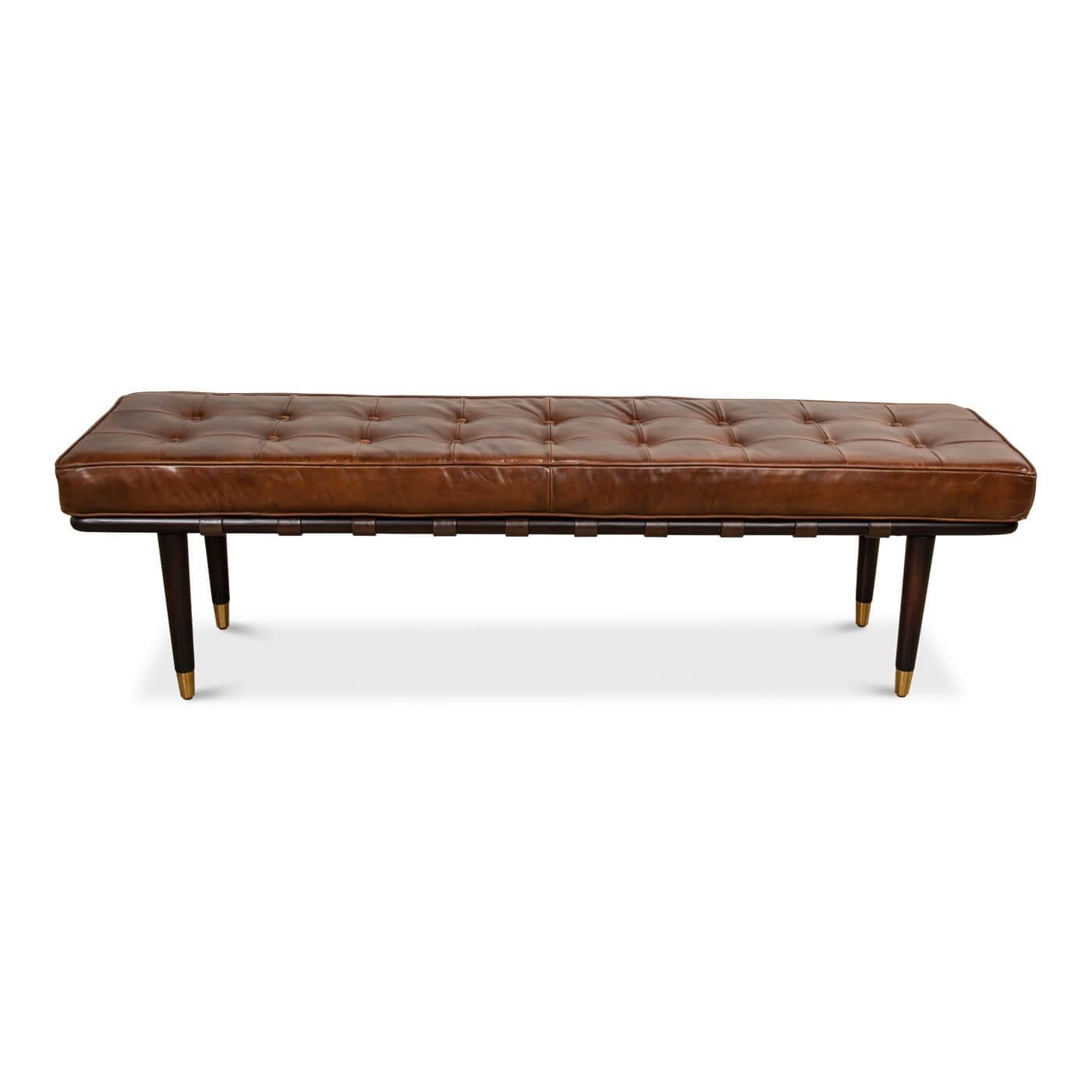 A Mid-Century Modern style tufted leather top bench. This boxed cushion benchtop is crafted in top grain leather in rich brown color with button tufting. It sits on four slender dark brown brass-capped wood legs. 

Dimensions: 64