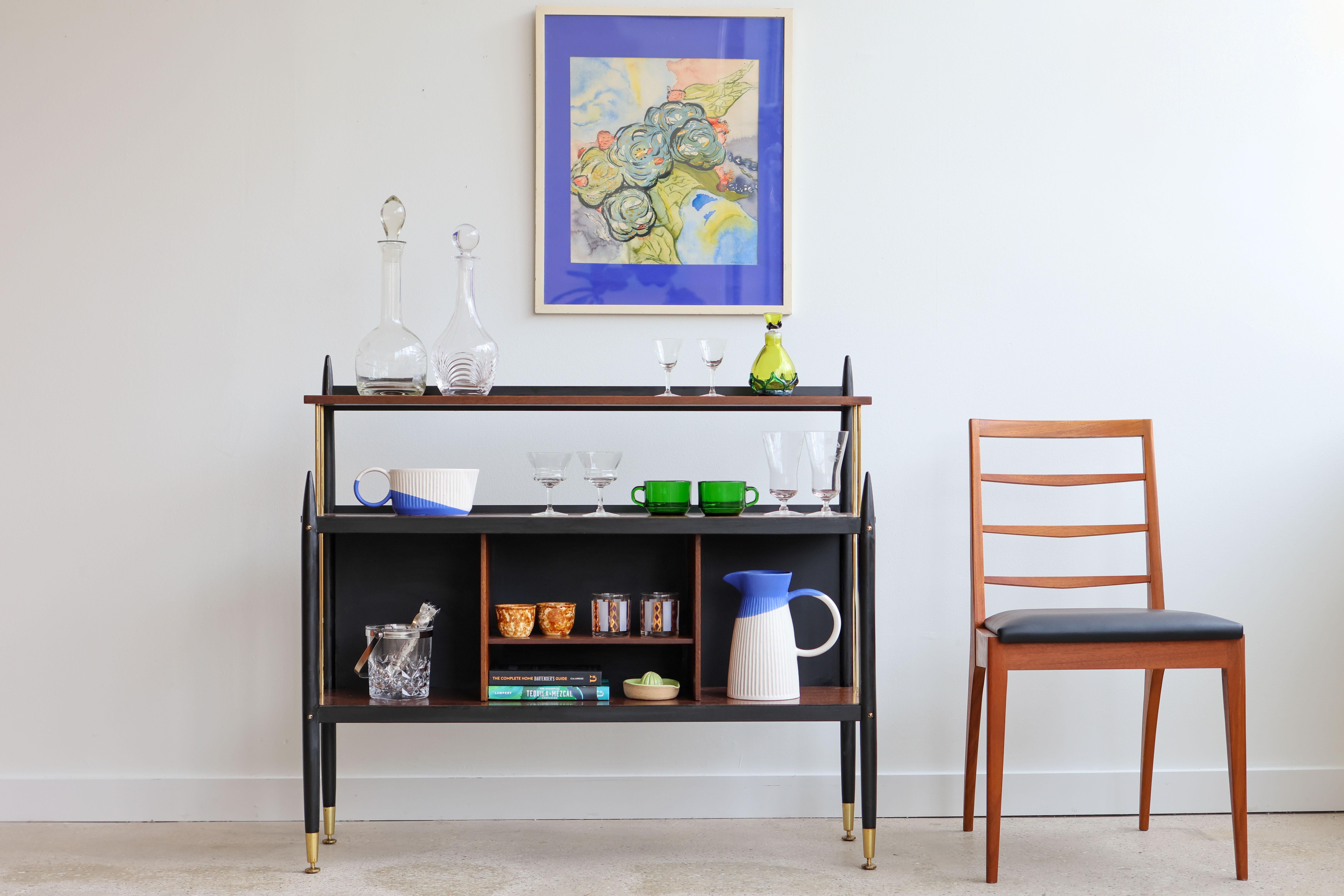 Mid-Century Modern tola bar display shelf unit.
From the 'Librenza' collection by G-Plan, UK, 1960s.
Tola wood (an African Mahogany) paired with ebonized wood and brass, inspired by late 1950s Italian glamour. 
Great as a serving bar or