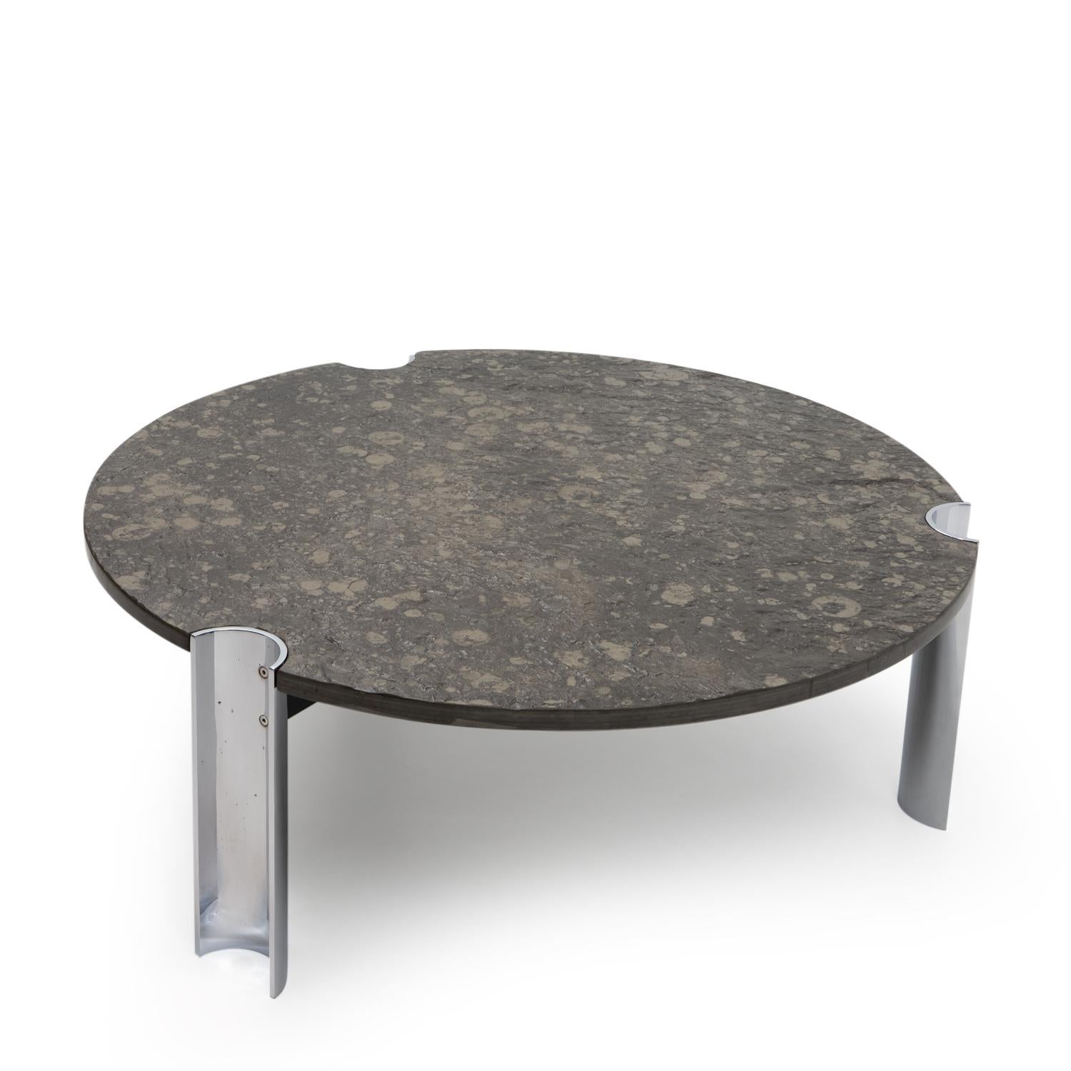Round, heavy coffee table dating from the 1970s and featuring a polished chrome steel base paired with a textured limestone top. 

The stone surface is embedded with an impressive array of prehistoric marine fossils, such as ancient sea snails—