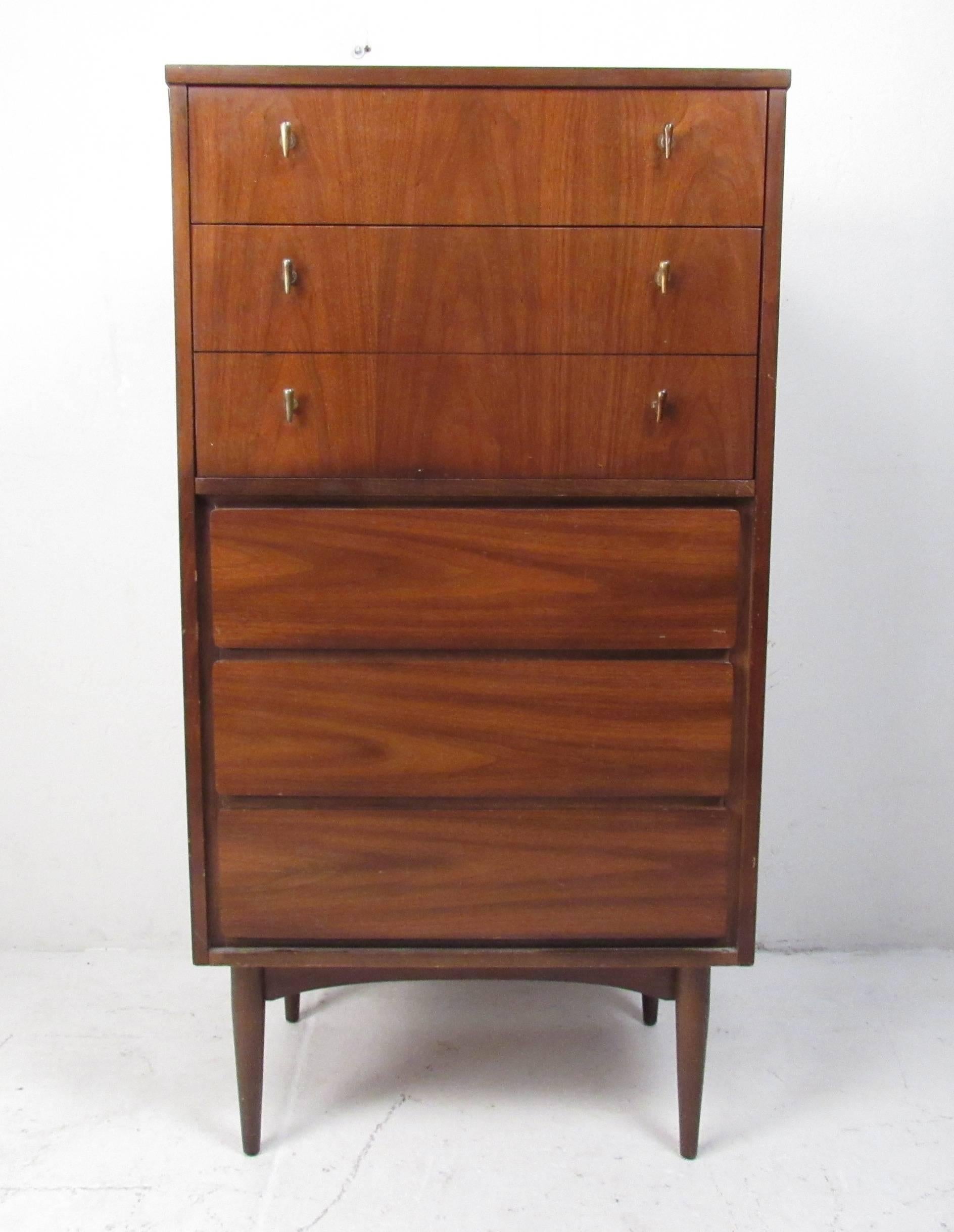 This stunning vintage modern tall chest has five hefty drawers with unique handles. Sleek design offers an abundance of storage space within a compact design. This well-made case piece has beautiful walnut wood grain throughout and sturdy tapered