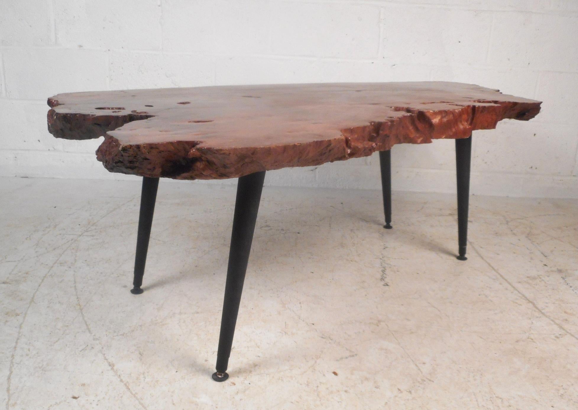 A wonderful vintage modern coffee table with a natural tree slab top and splayed black legs. This unique table features live edges and a sleek lacquered finish on the top. This large rustic style coffee table makes the perfect eye-catching addition
