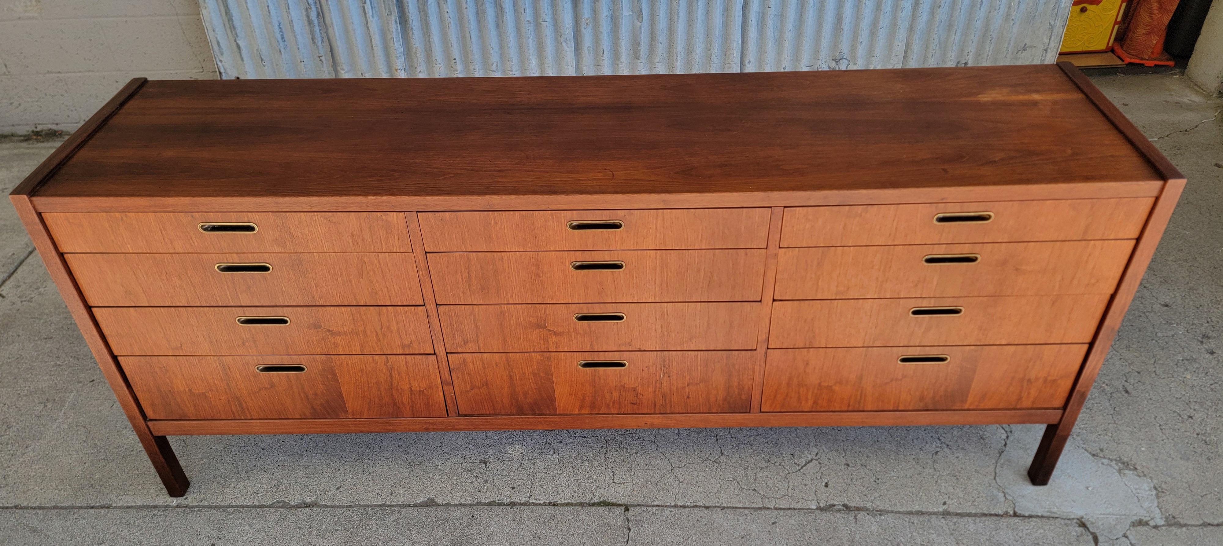 An oversized low Mid-Century Modern walnut dresser with 12 drawers. Fine craftsmanship and materials. Solid oak interior wood with dovetail construct at front and back of drawers. Dust panels between drawers and wooden center glide track. Drawers