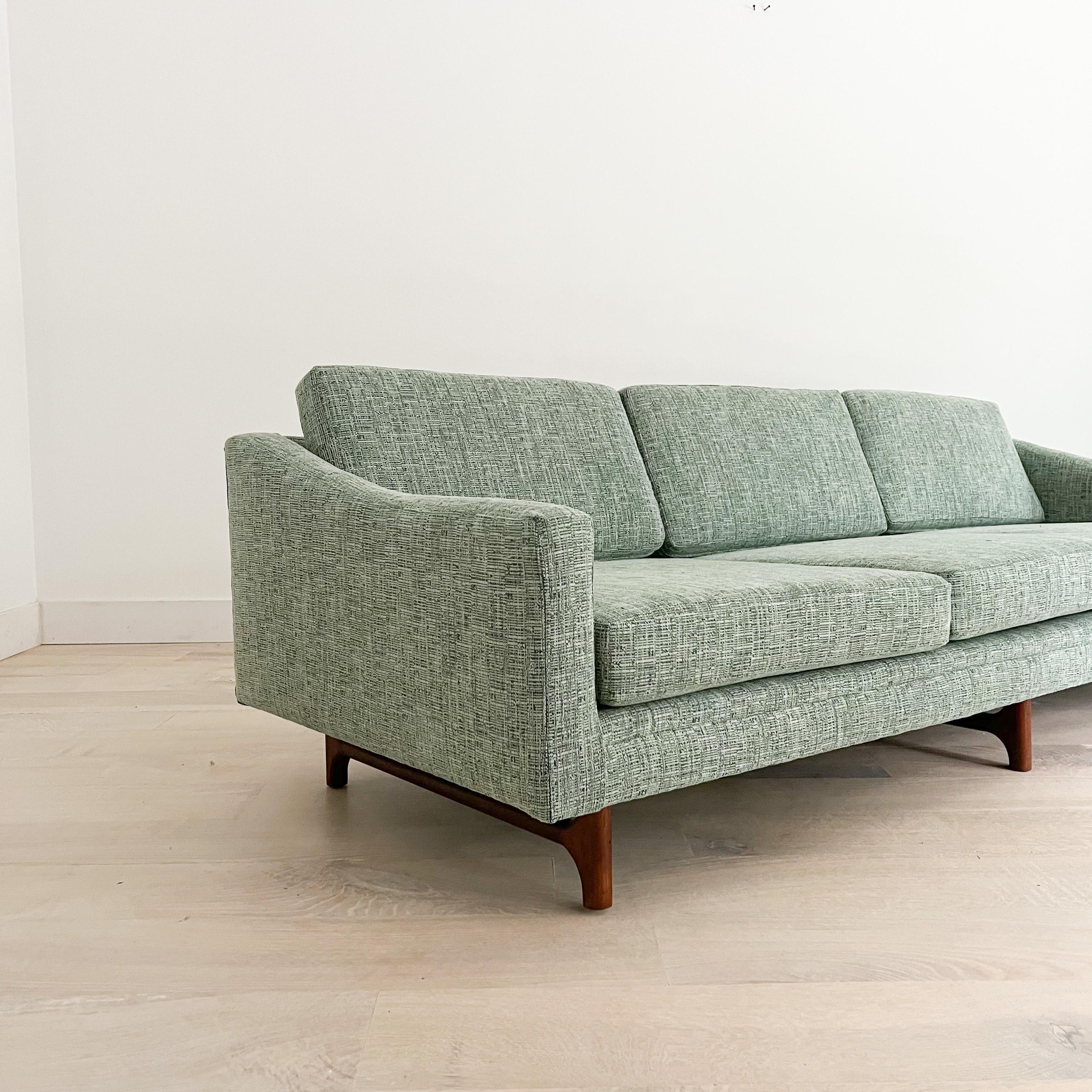 Mid-Century Modern low and long three seater sofa manufactured by Rowe Furniture. Circa 1960s. All new foam and light teal upholstery. Stunning sculpted walnut legs.