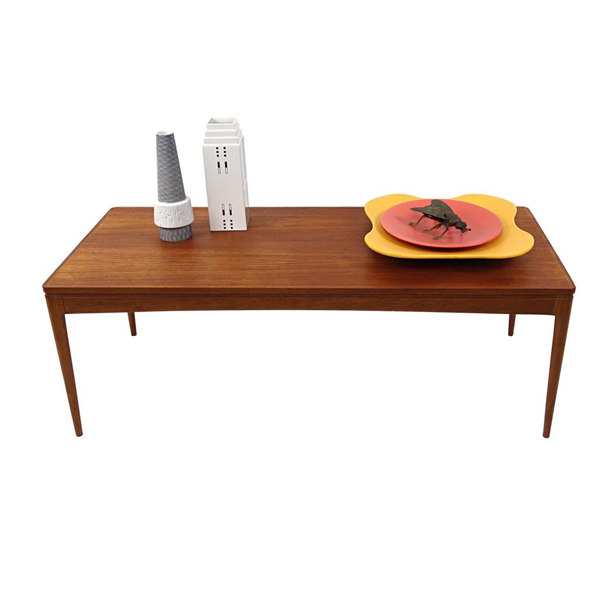 This elegant teak wood coffee table radiates homeliness in its simplicity. The rounded edges of the table top can also be found in the rounded shape of the top at the pint where the legs start. This gives the table a soft tone and together with the