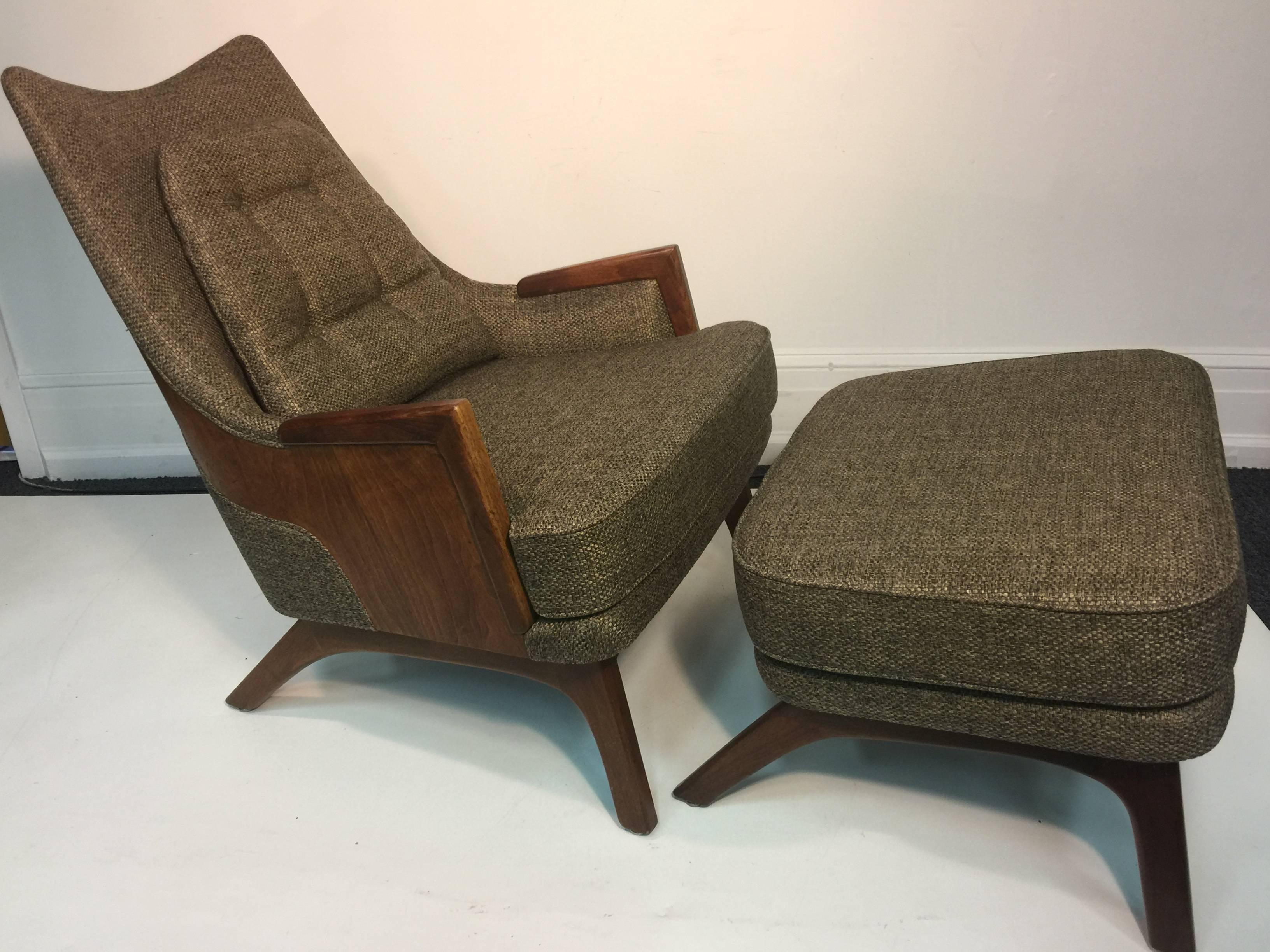 Great aerodynamic design armchair with ottoman upholstered in a beautiful brownish oatmeal woven fabric with button tufted removeable back pillow with a deep walnut back, angled legs and arms. There is the substantial matching four legged ottoman
