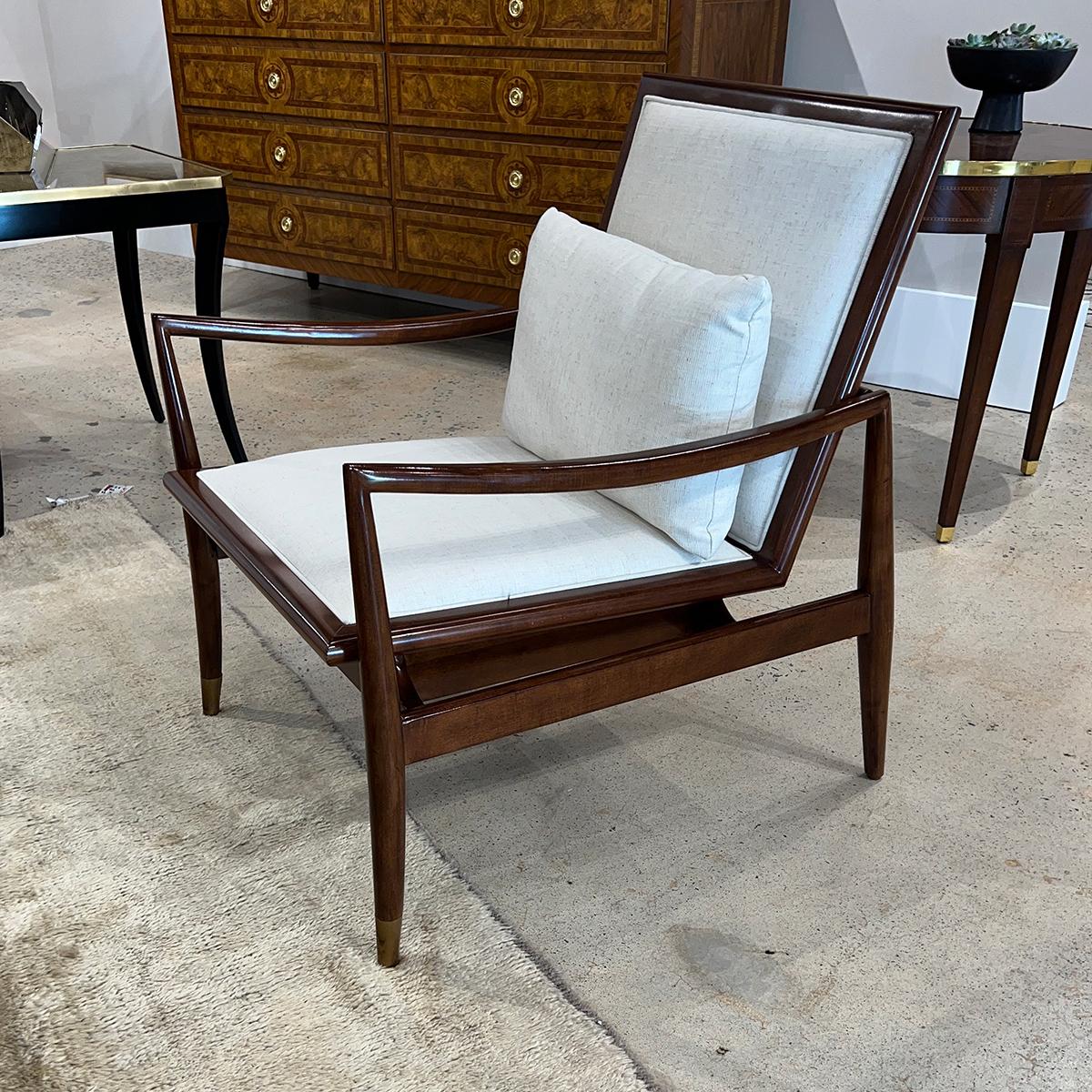 In a warm brown polished walnut finish. With an upholstered cushion backrest and seat in a Linen performance fabric. 

The classic modern and graceful frame with an angled back and swooping arms, with brass caps to the legs.

Dimensions: 26