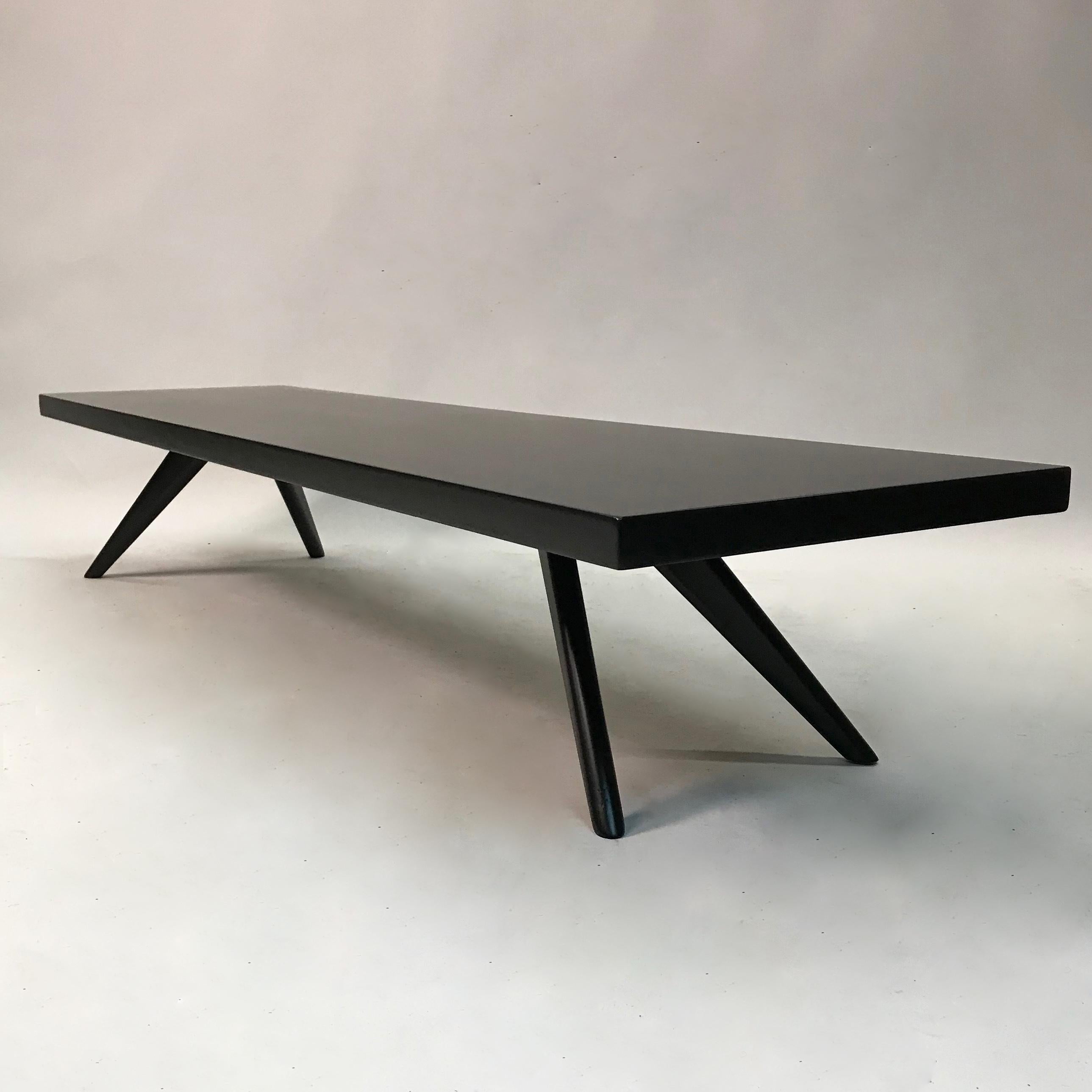 Mid-Century Modern, black lacquered mahogany, coffee table features a sleek profile with a long, low rectangular top and splayed, tapered legs.