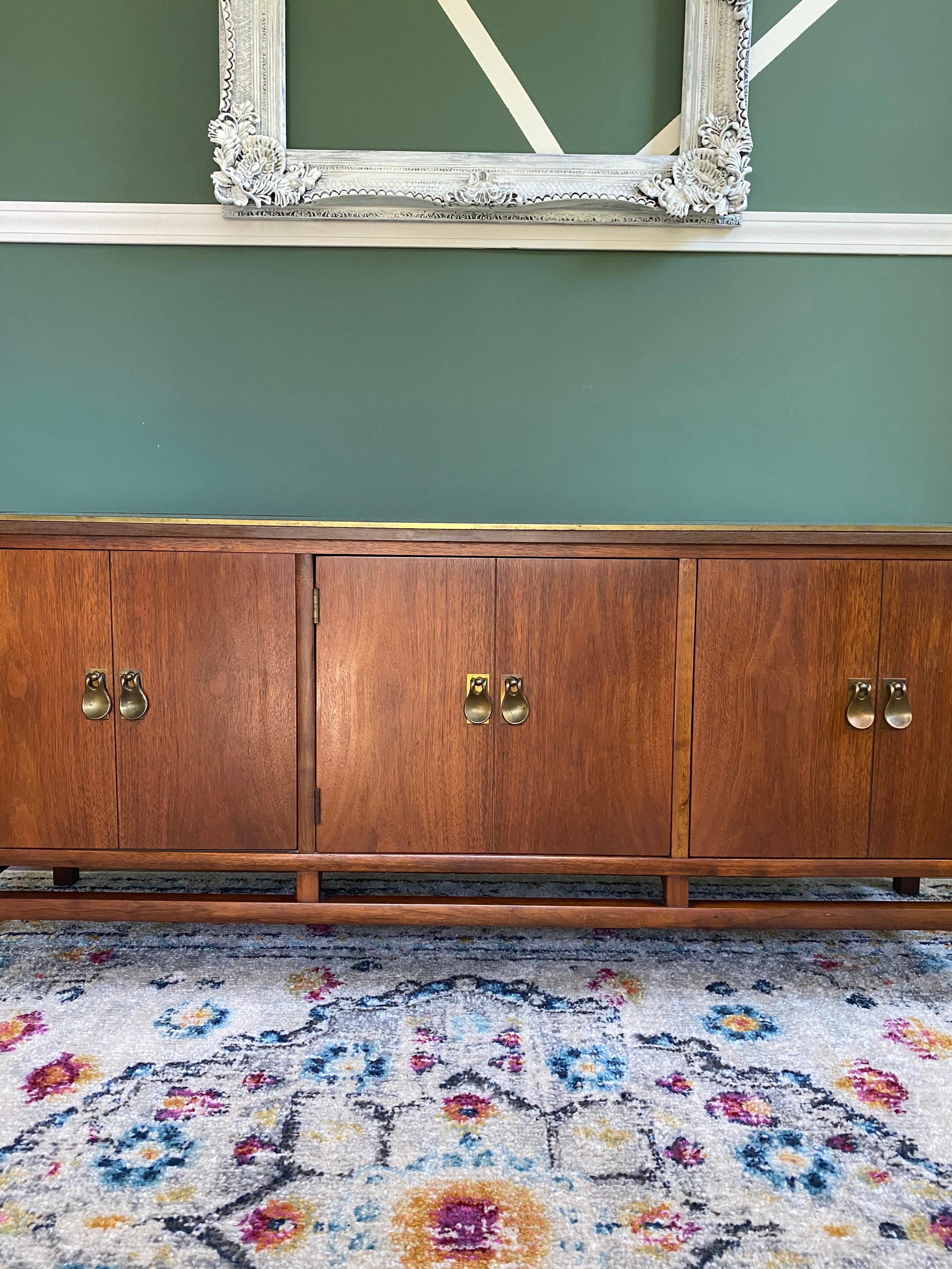 Beautiful 3 cabinet Mid-Century Modern low credenza with brass handles, beautiful legs and brass corners with a laminate top. Brass corners have a few imperfections and left cabinet as some trouble opening.