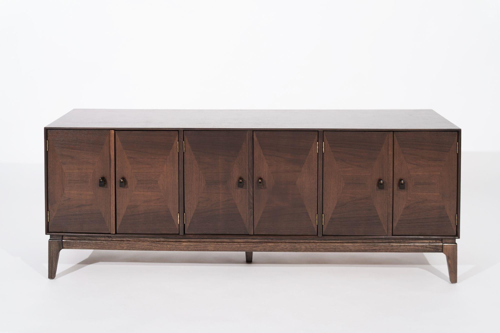 A completely restored low-profile credenza or media unit, circa 1950-1959. The doors open up to reveal shelving. The door-knocker-style hardware has been refinished in ORB.