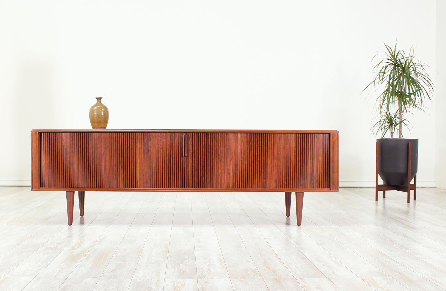 Mid-Century Modern Tambour Door Credenza designed and manufactured in the United States by Barzilay in the 1960’s. Low in profile, this beautifully refinished walnut storage unit is accented with inconspicuously slatted door pulls for functional