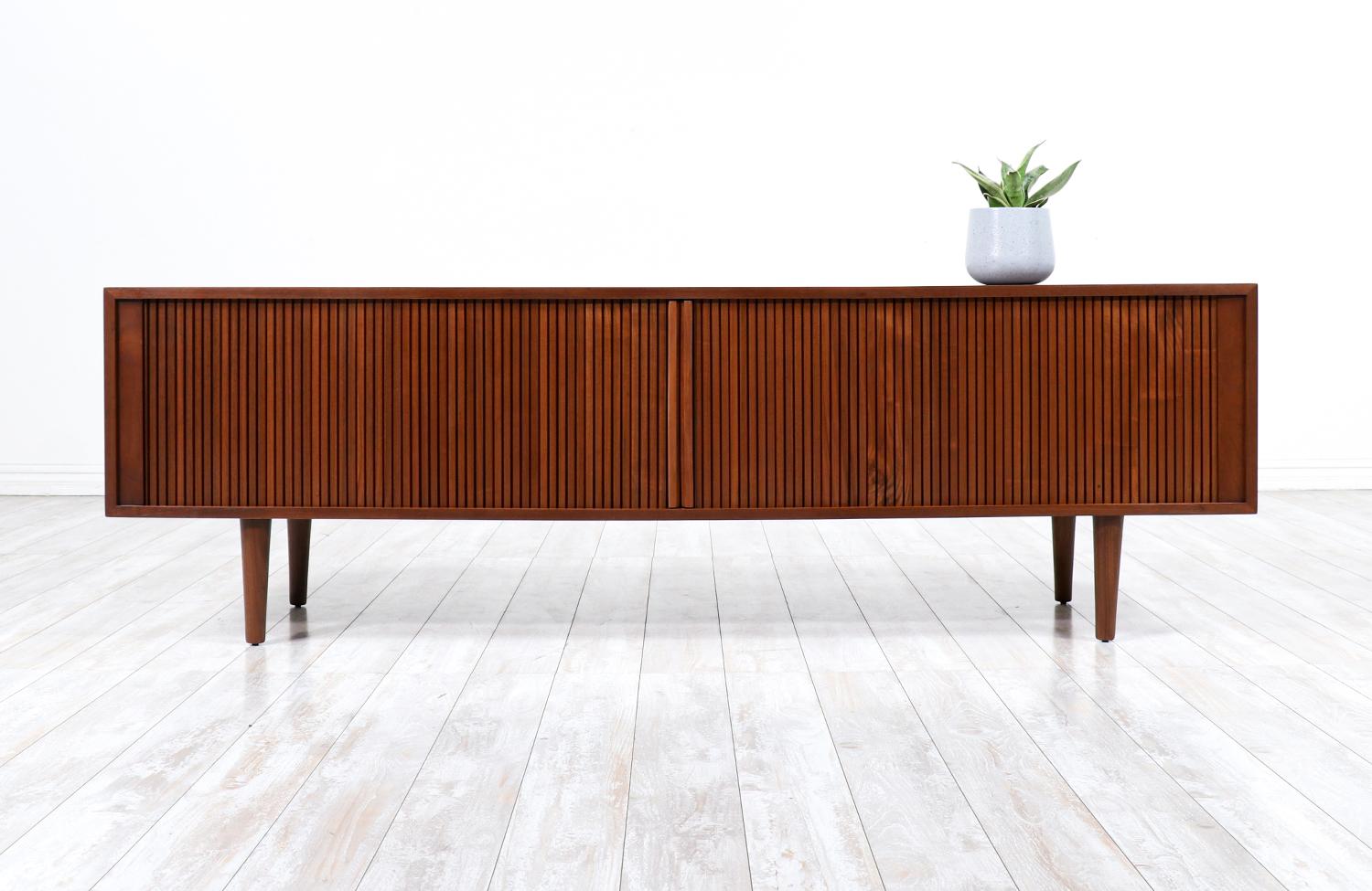 Mid-Century Modern Tambour Door Credenza designed and manufactured in the United States in the 2010’s. Low in profile, this beautifully refinished walnut storage unit is accented with inconspicuously slatted door pulls for functional ease. With