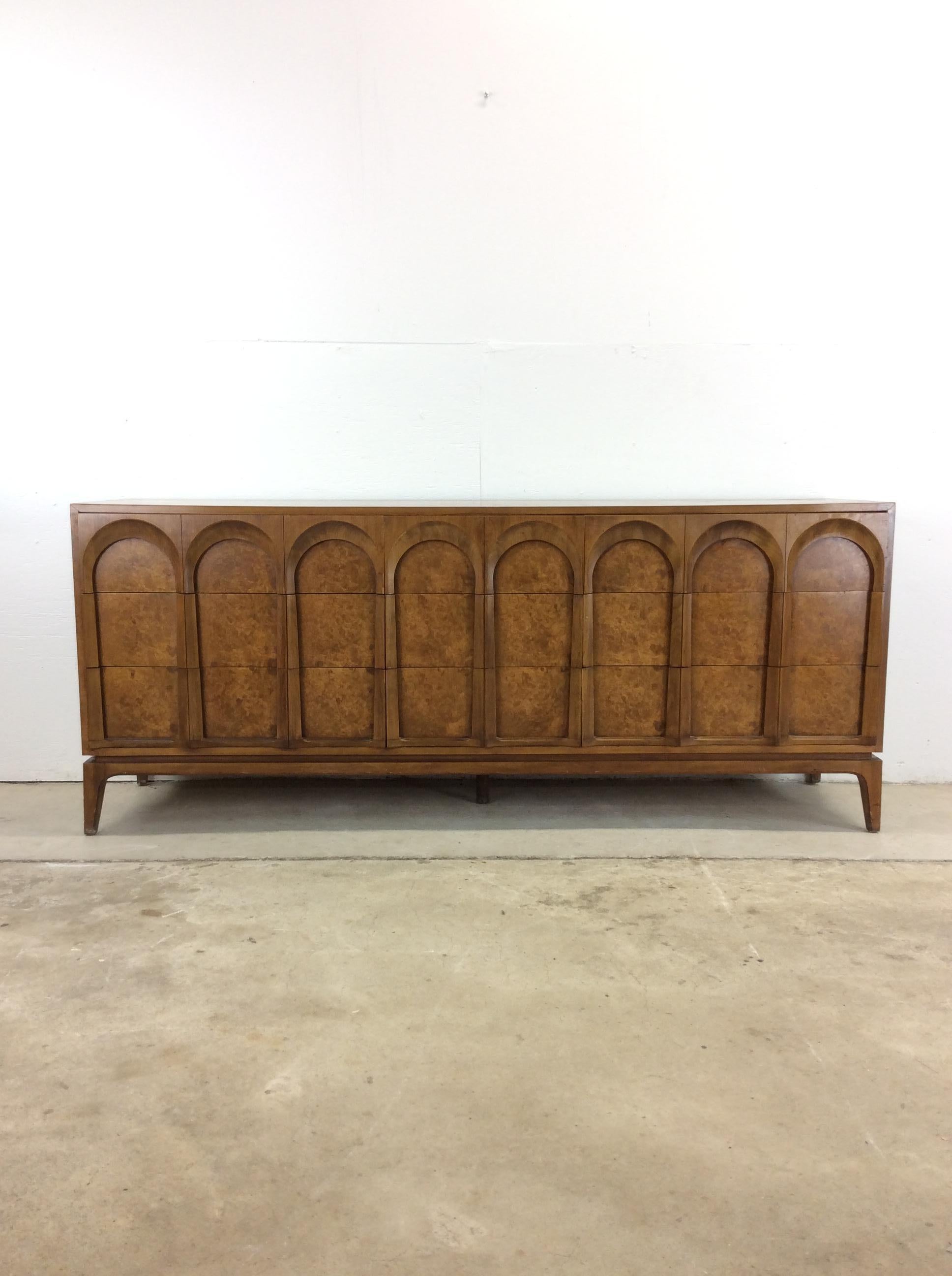 This mid century modern lowboy dresser by Thomasville features hardwood construction, beautiful burlwood veneer with original finish, nine dovetailed drawers with unique arched detail, and tall tapered legs.   Matching pair of nightstands and