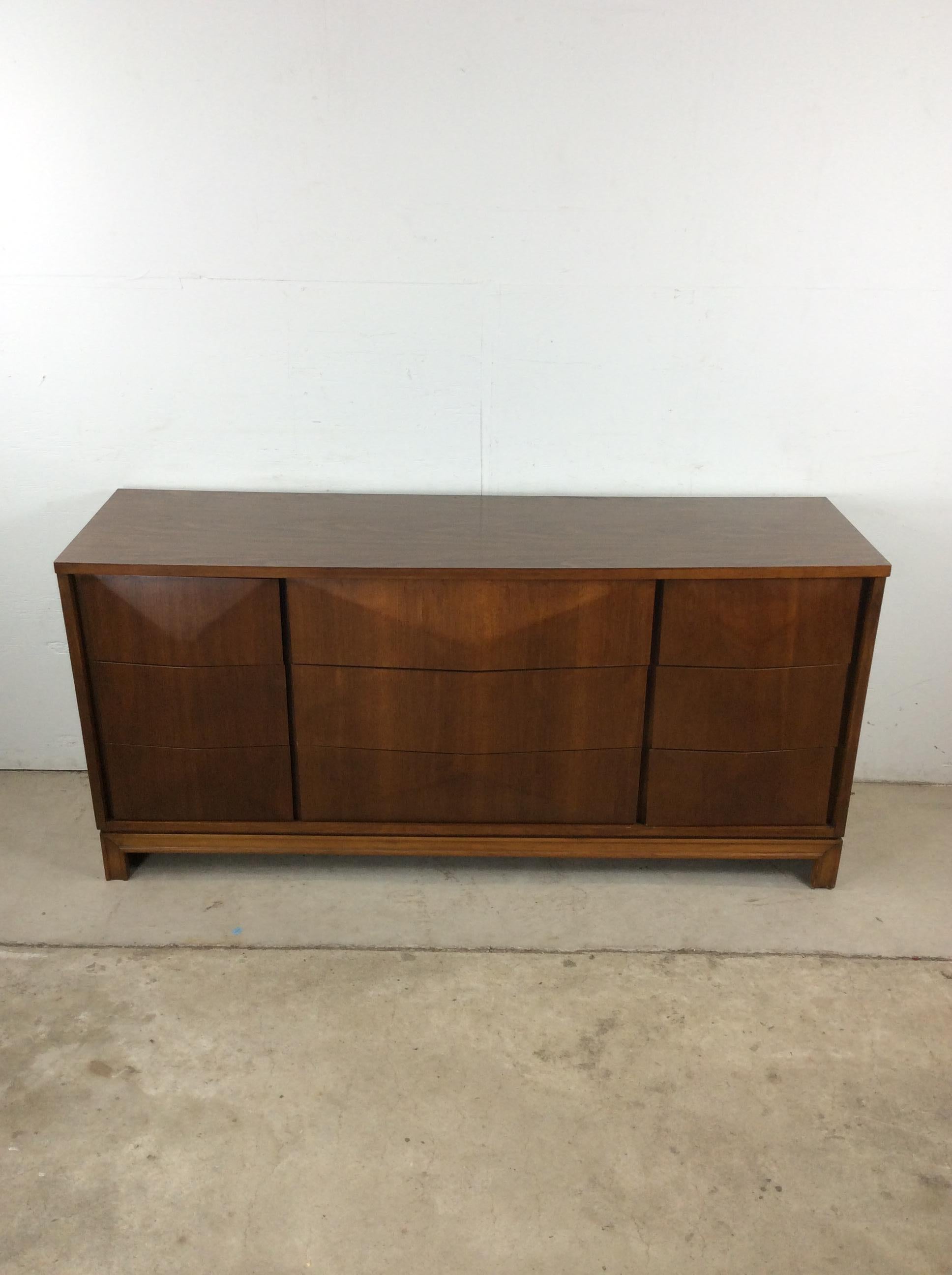 Questo comò basso moderno di metà secolo di Johnson Carper presenta una struttura in legno massiccio, impiallacciatura in noce con finitura originale, nove cassetti a coda di rondine con frontali smussati, gambe scolpite e un resistente piano in