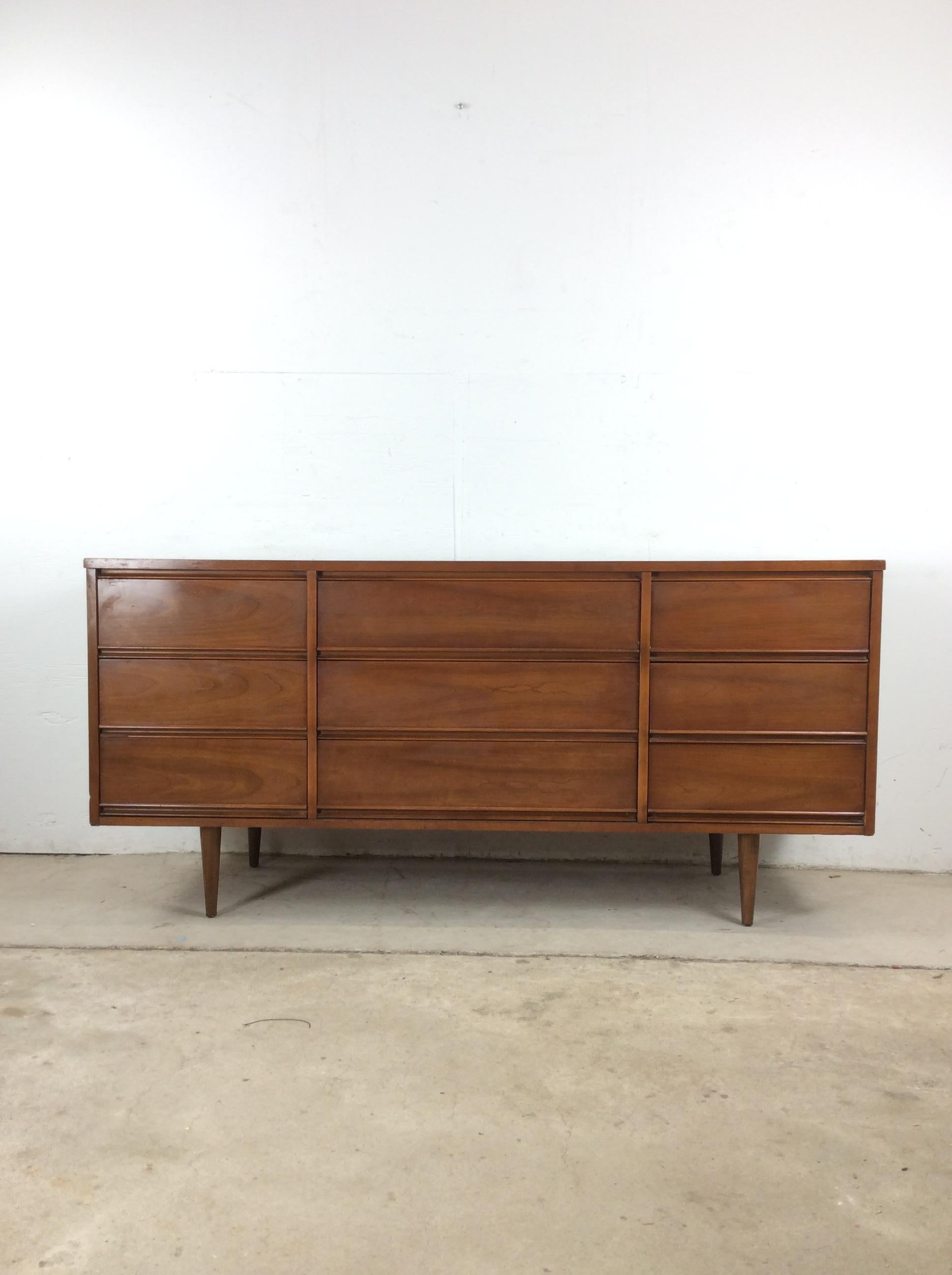 Questo comò basso moderno di metà secolo presenta una struttura in legno massiccio, impiallacciatura in noce con finitura originale, nove cassetti a coda di rondine con tiretti in legno intagliato e alte gambe affusolate. u2028u2028Il comò Highboy