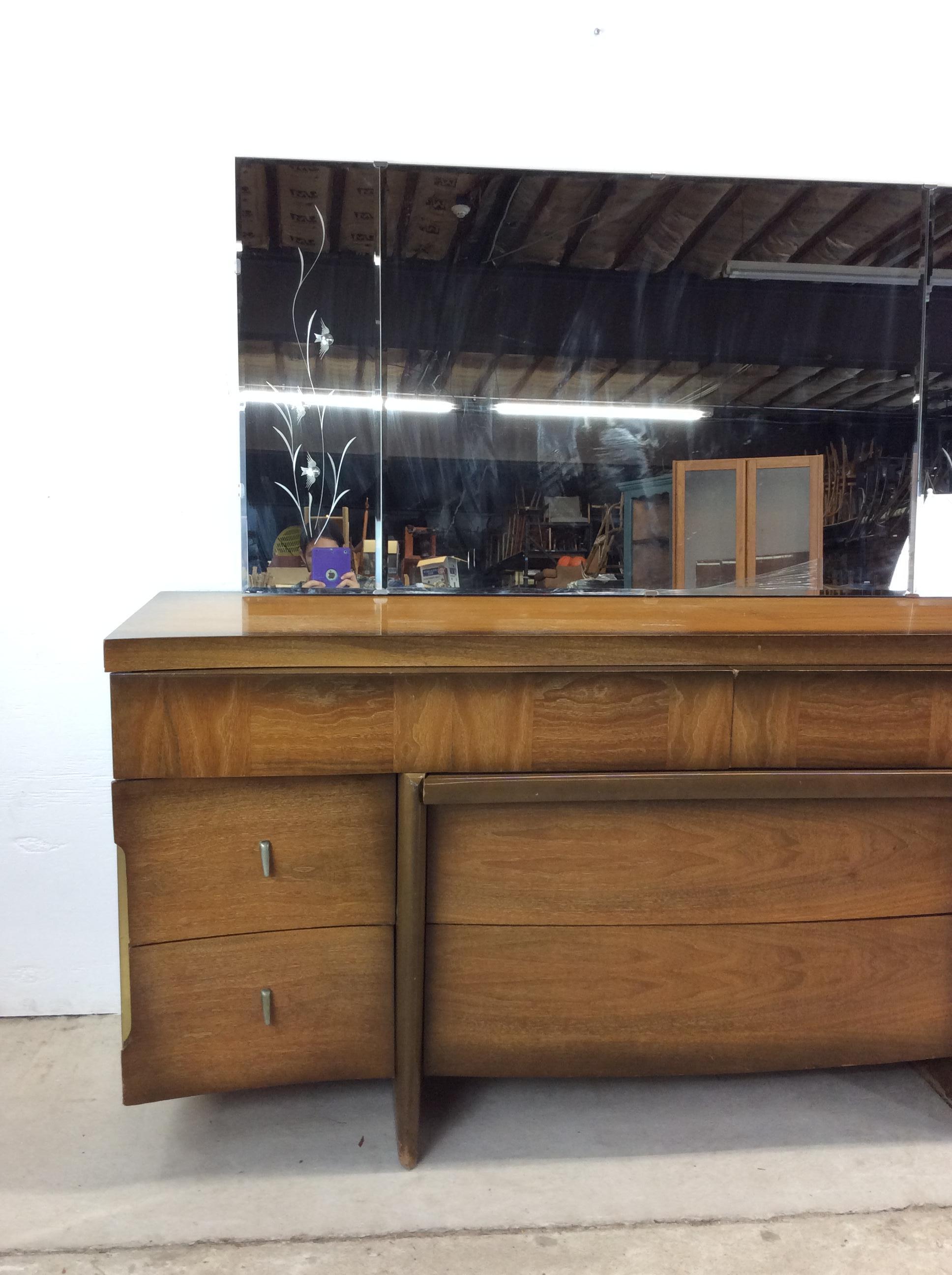 This mid century modern lowboy dresser features hardwood construction, walnut veneer with original finish, 8 dovetailed drawers with brass hardware, unique sled legs, and a large mounted mirror with beveled glass.  Mirror height 30.5 inches