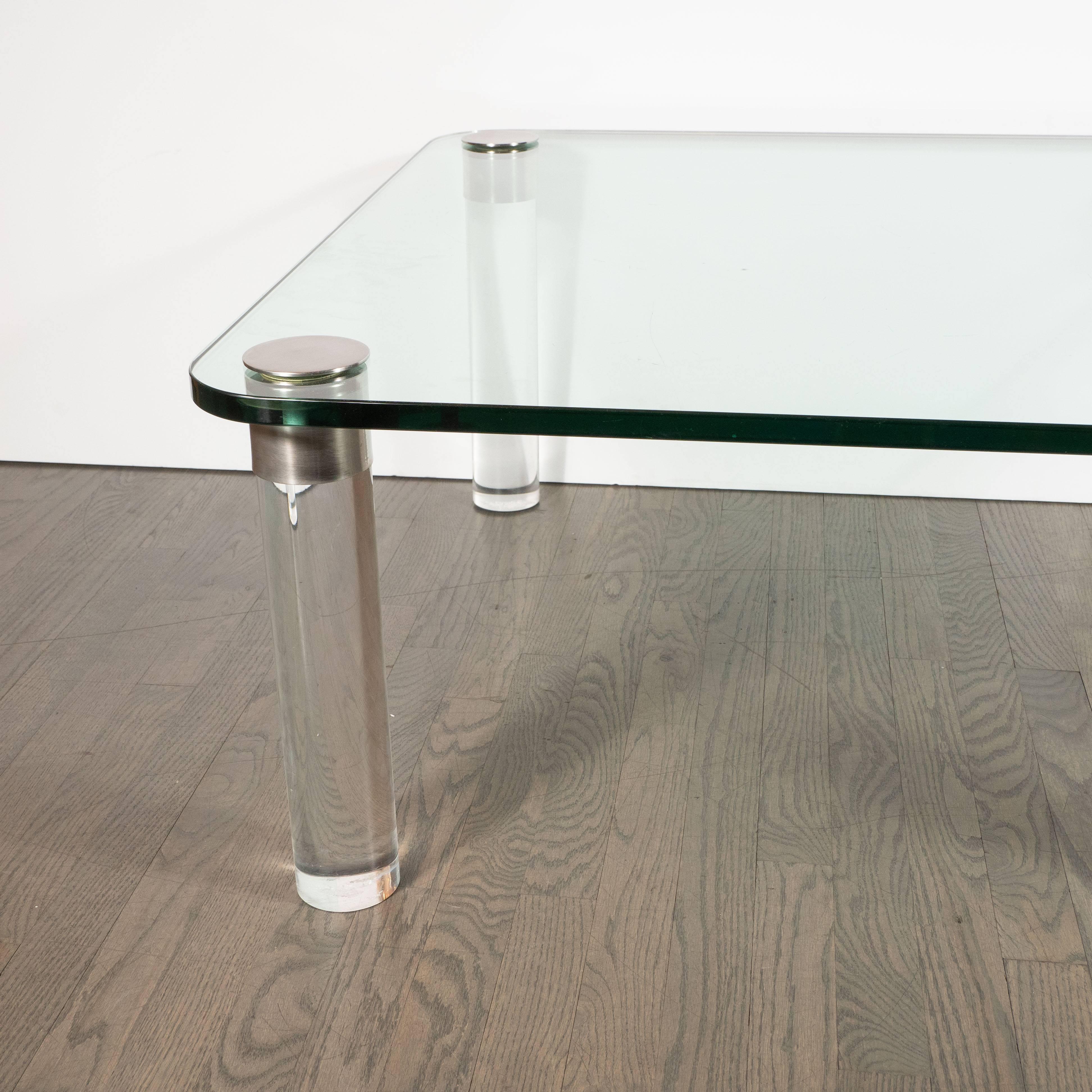 This refined glass and Lucite cocktail table was realized in the United States, circa 1970. Designed by Leon Rosen the founder of the esteemed Pace collection, circa 1970, this stunning table features cylindrical Lucite feet topped with brushed