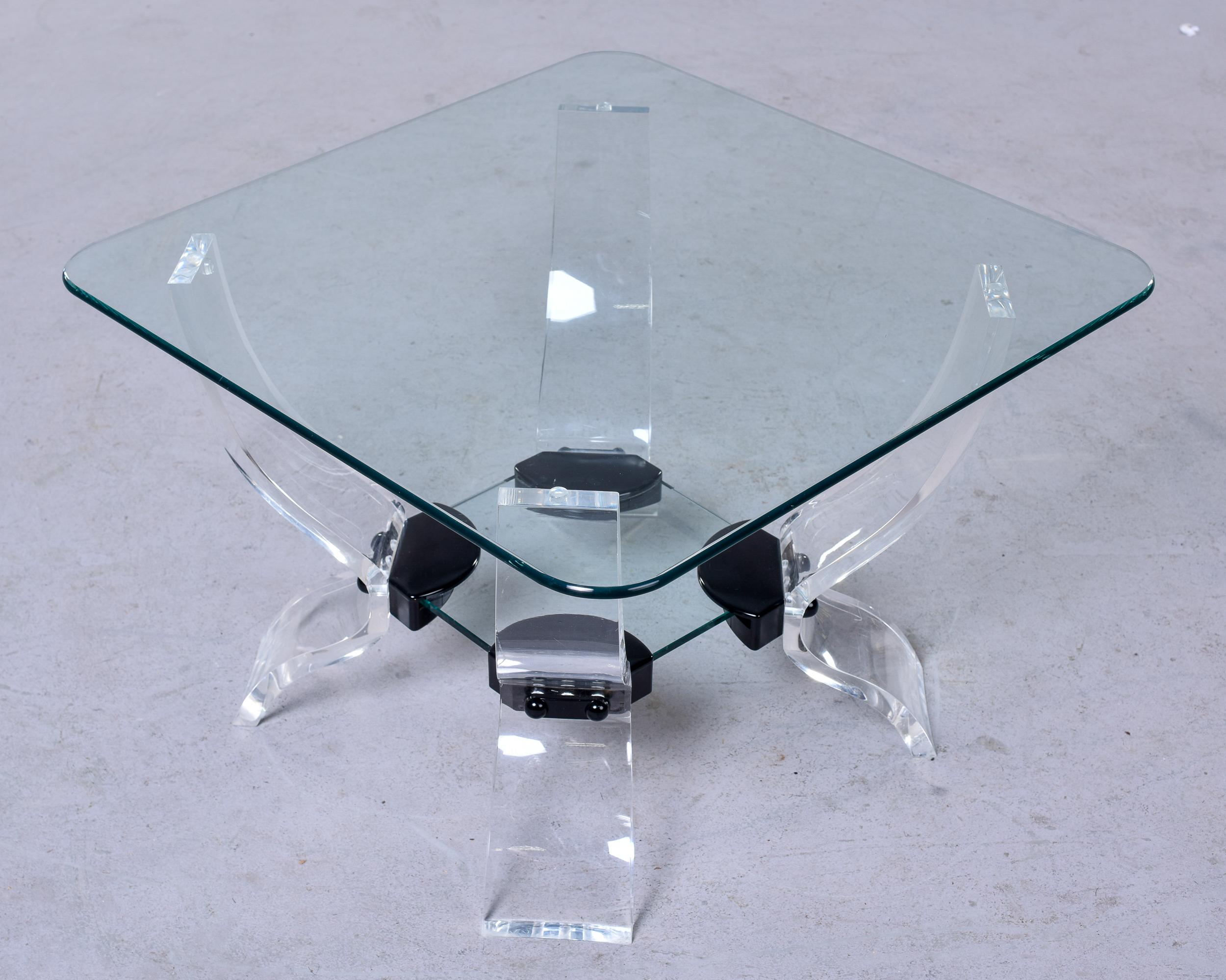 Found in France, this circa 1970s side table features a curvy four leg base in clear lucite with black accents. There is a lower level small glass shelf and the top is 1/2” thick clear square glass with rounded corners. Unknown maker. 

Very good
