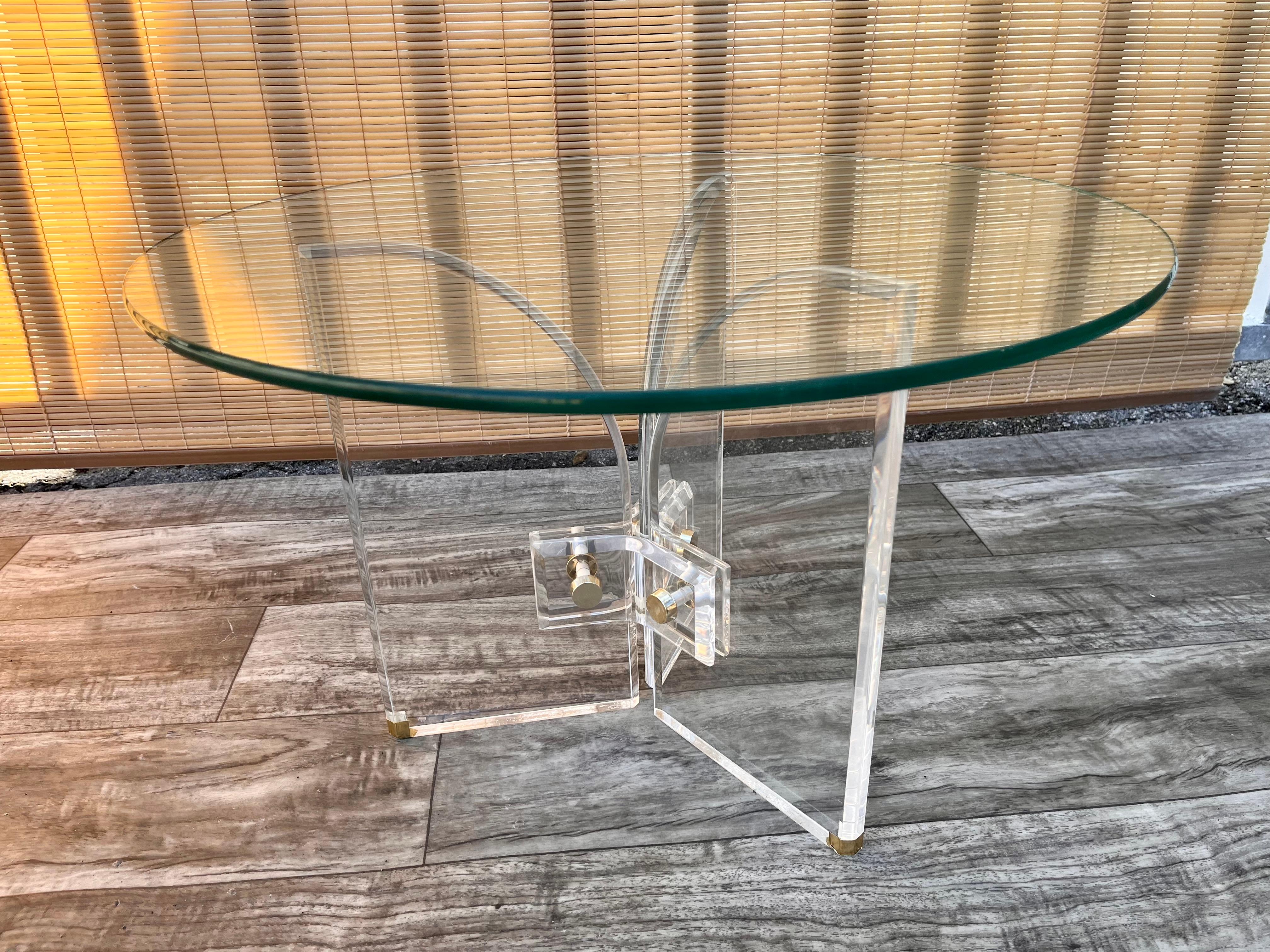Vintage Mid-Century Modern Lucite Arches side table in the manner of Charles Hollis Jones. Circa 1970s
Features a round glass top, three lucite arched panels connected with lucite brackets, bolted throughout and capped with brass color caps. 
In