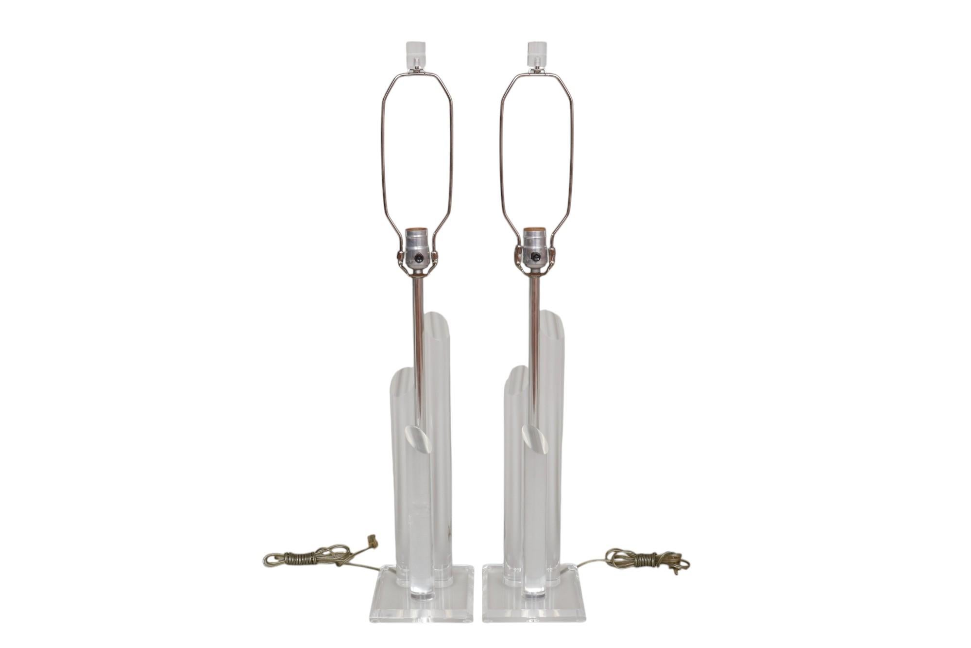 Coppia di lampade da tavolo in lucite trasparente della metà del secolo scorso. Le colonne centrali cromate sono affiancate da tre pilastri cilindrici in lucite. Posizionato su una base quadrata in lucite smussata. Le lampade sono dotate di paralumi