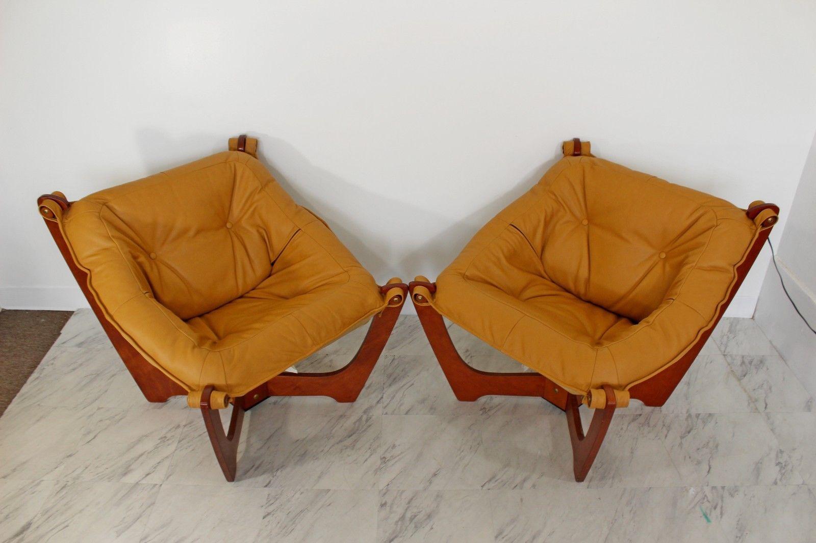 For your consideration is a pair of Luna Sling chairs are made of birch plywood with a warm natural tone. The four legs come out of a square base on an angle with soft curves leading upward. The seating is covered in tan leather and attaches to the