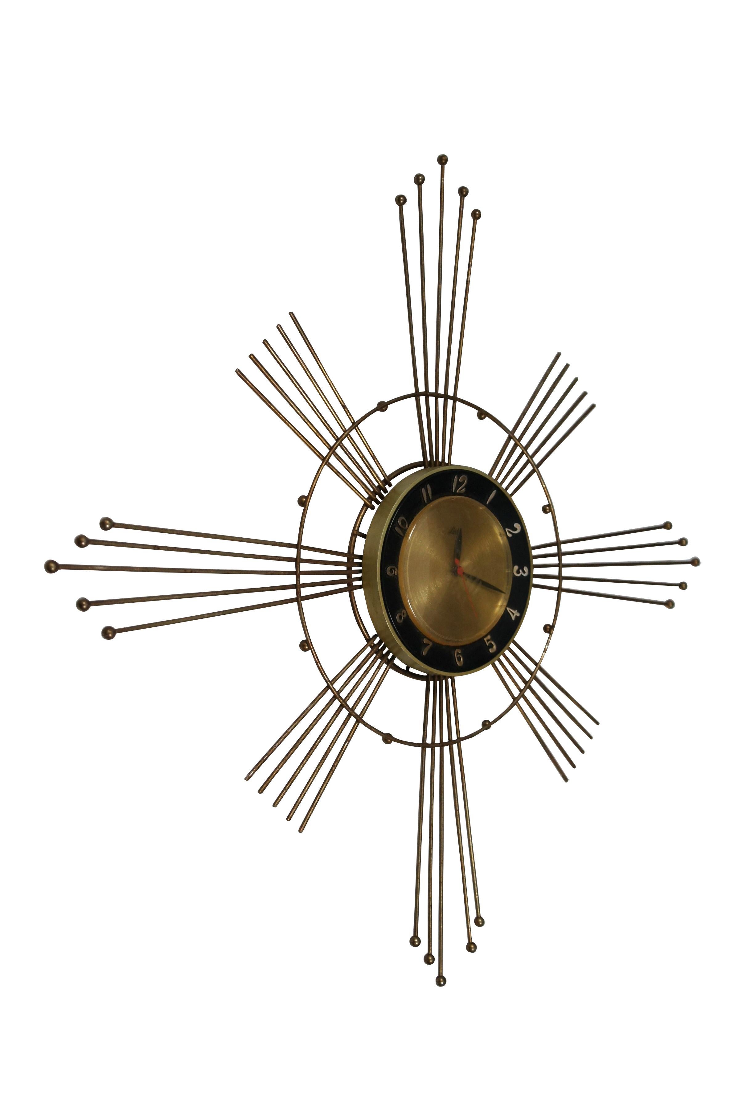 Mid 20th century electric / plug in wall hanging clock. Mid century modern / atomic brass sunburst / starburst with graduated rays and circular frame accented with brass balls. Gold tone plastic face with black frame; gold Roman numerals; black