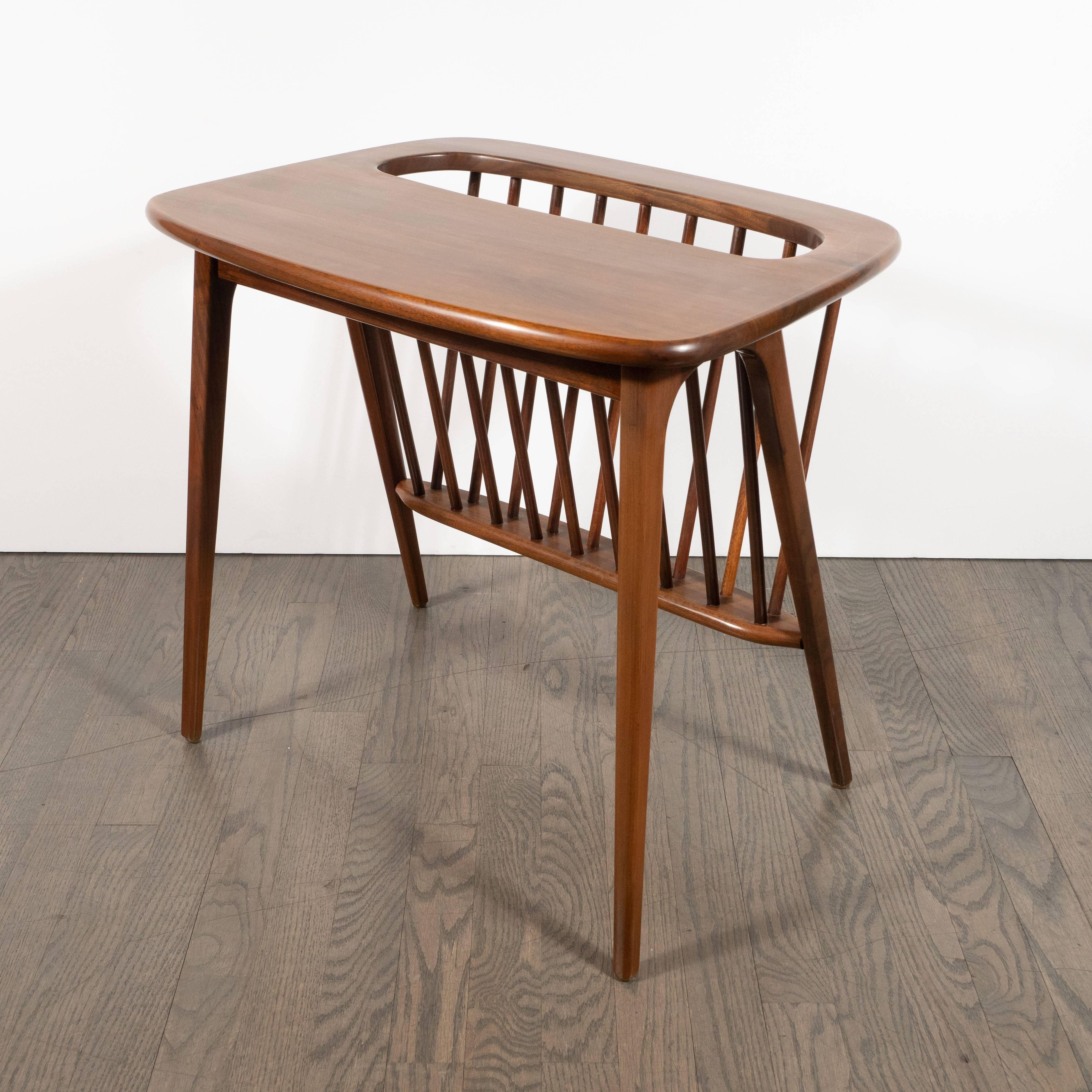 This elegant and graphic Mid-Century Modern hand rubbed book matched walnut magazine holder/ side table was realized in the United States, circa 1960. It features splayed legs of divergent angles that connect at a curvilinear U-form joint that