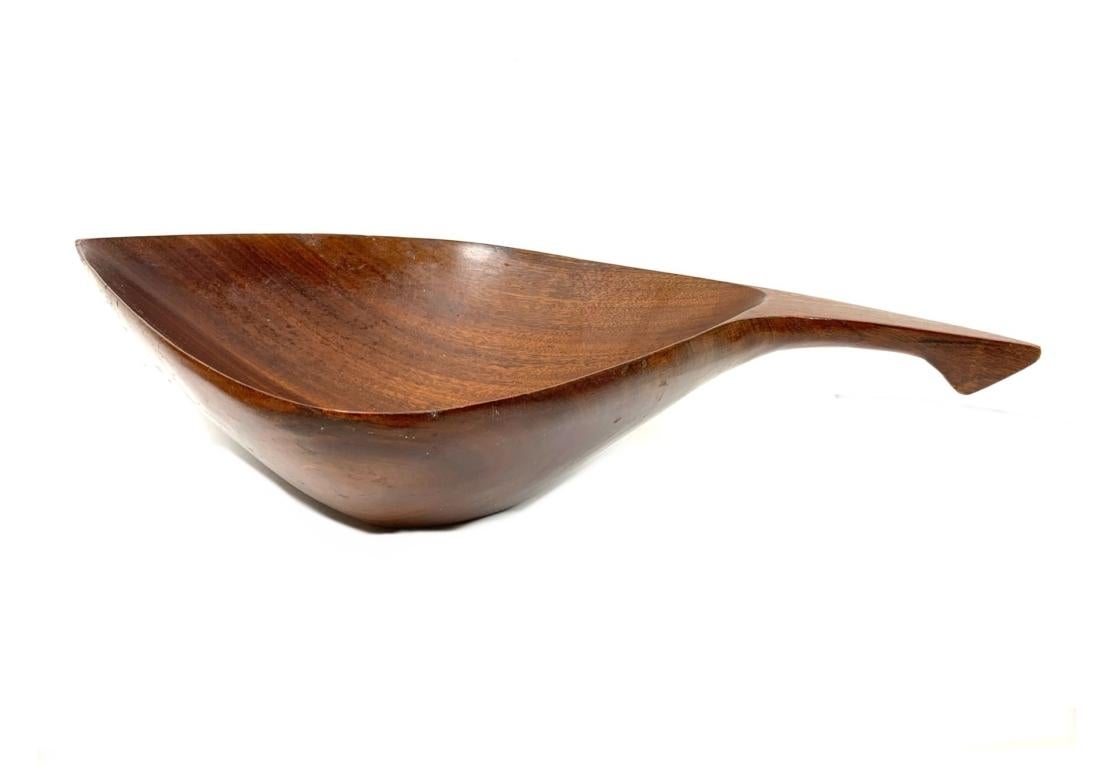 A Mid Century Modern  solid mahogany bowl with handle and serving utensils. Attributed to Arthur Umanoff who designed a variety of mahogany handled bowls and serving trays, primarily as part of his 