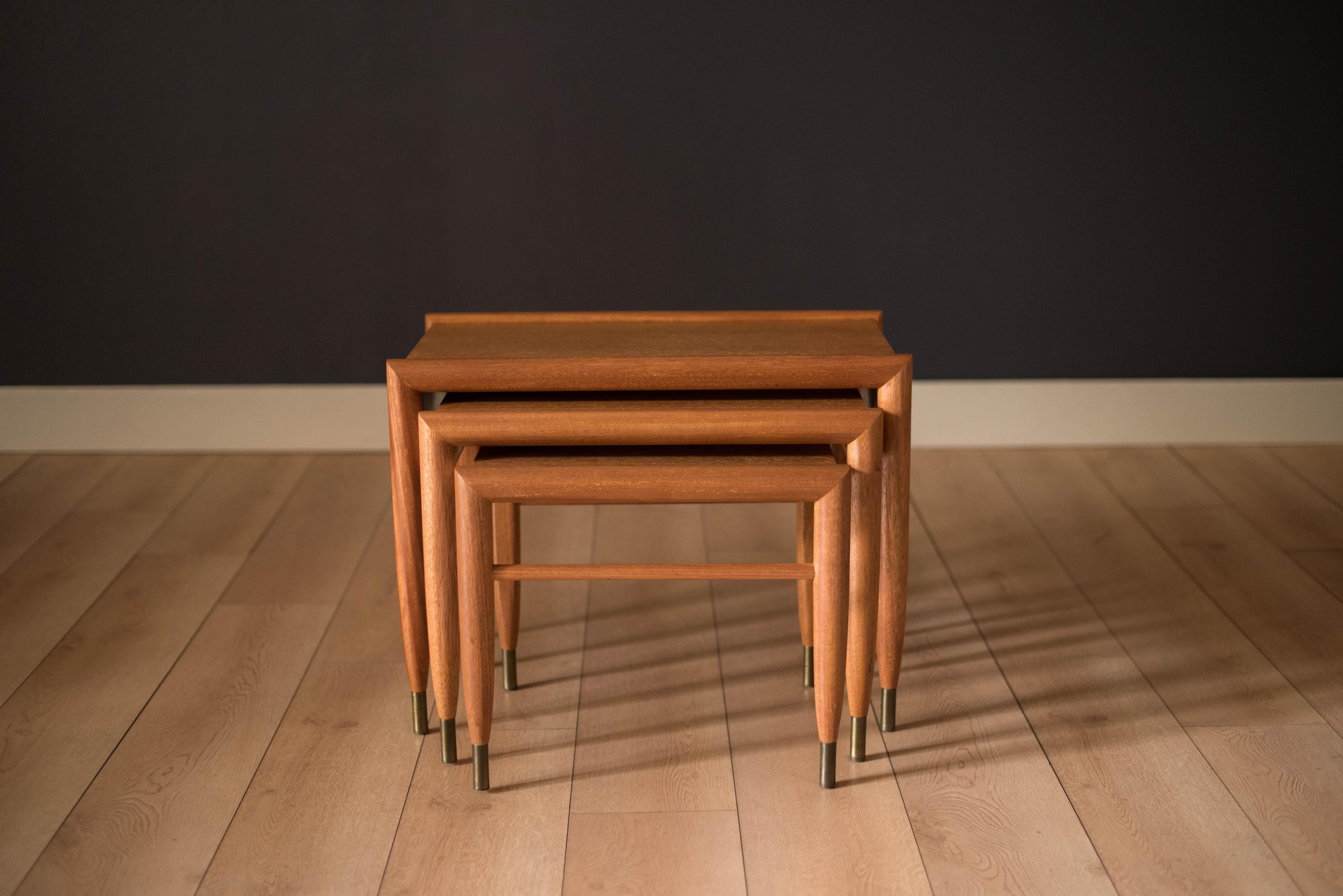 Vintage set of three nesting side tables by John Keal for Brown Saltman in mahogany, circa 1950s. This versatile set features a rounded edge detail that taper into the legs complete with brass tips. Includes three separate end tables that cleverly