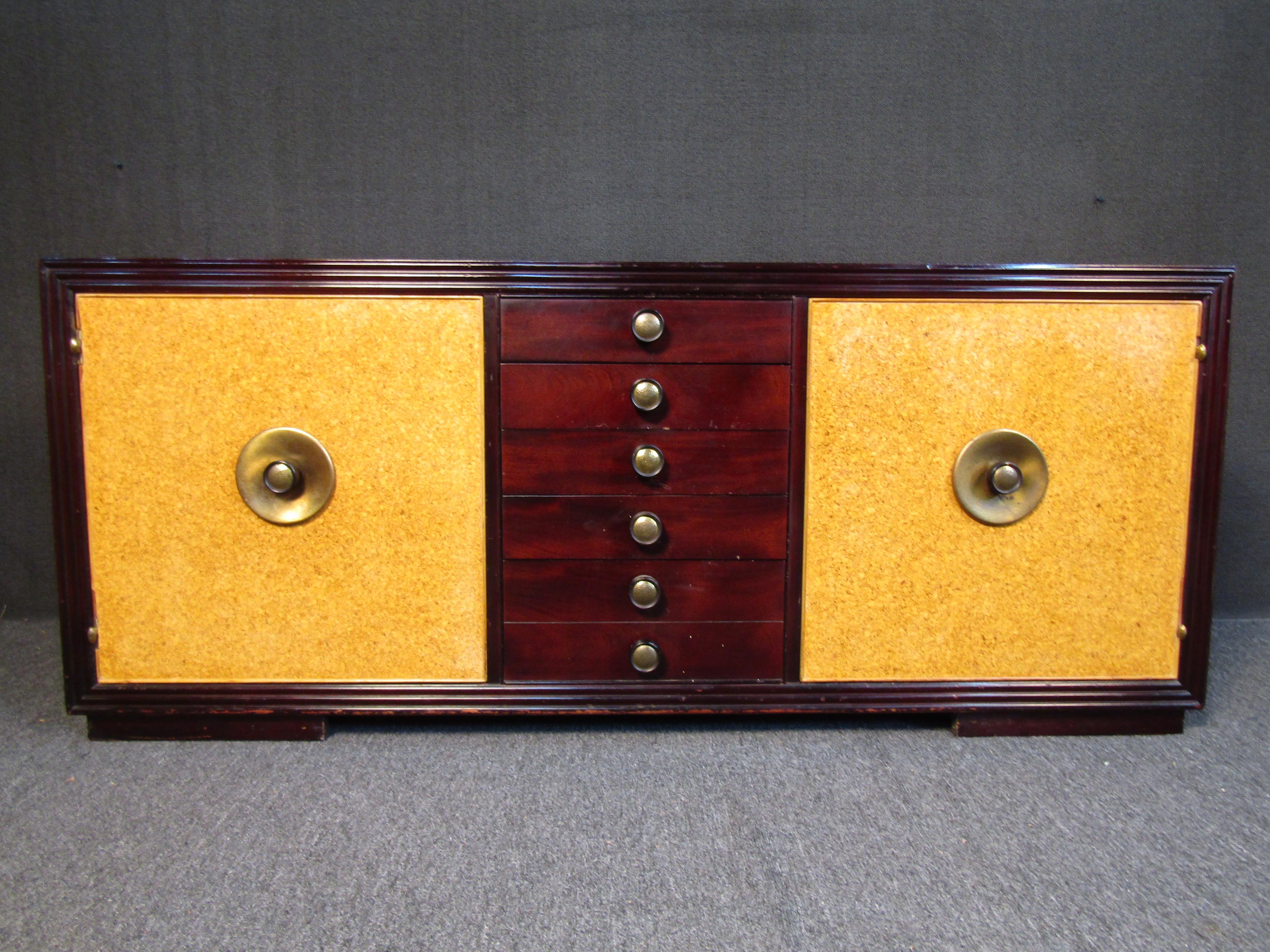 Paul Frankl for Johnson Brothers credenza featuring mahogany veneer, cork laminated doors and brass hardware. inside the left door holds 4 dovetail jointed drawers, right door contains 2 shelves. Designed by John Stuart.

(Please confirm location