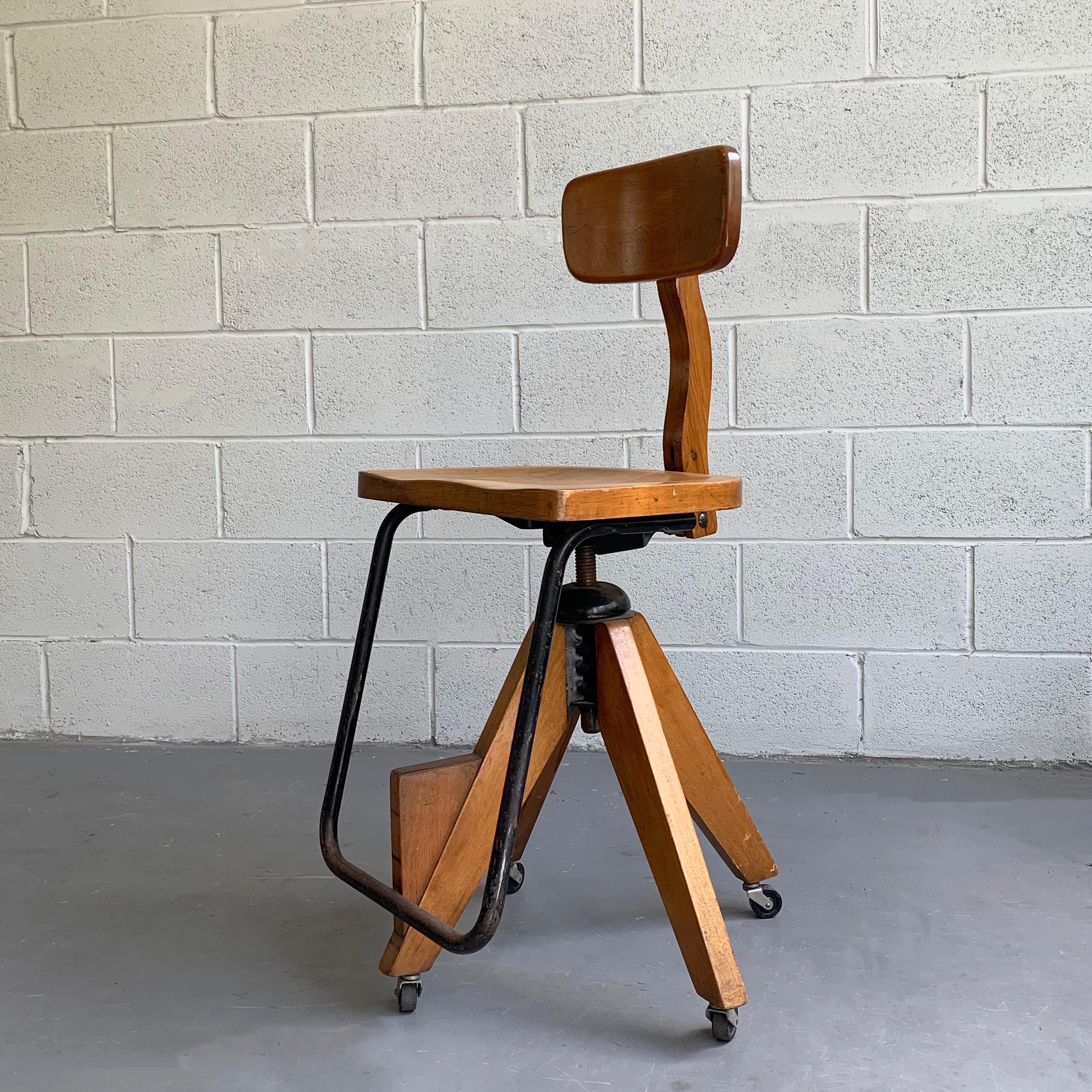 Stylish, Mid-Century Modern, maple, rolling, drafting stool in the style of Jean Prouve features an elongated, iron footrest, contoured, swivel seat at 17 inches wide x 13 inches deep and height adjustable from 22 - 27 inches.