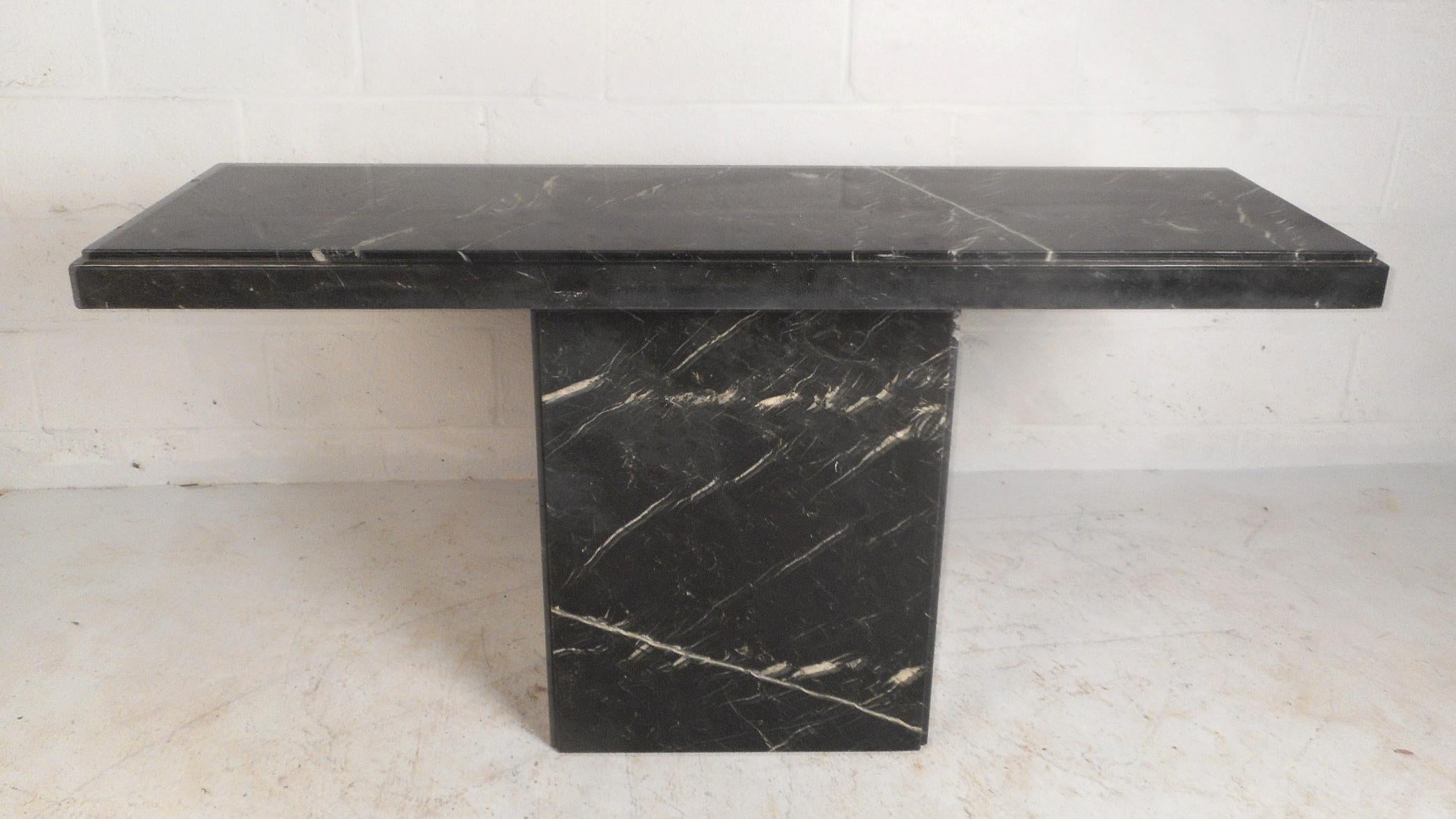 This stunning vintage modern console table features a black marble pedestal base with a rectangular black marble slab top. An elegant piece that looks amazing in any entryway, hallway, or behind the sofa. The unusual 