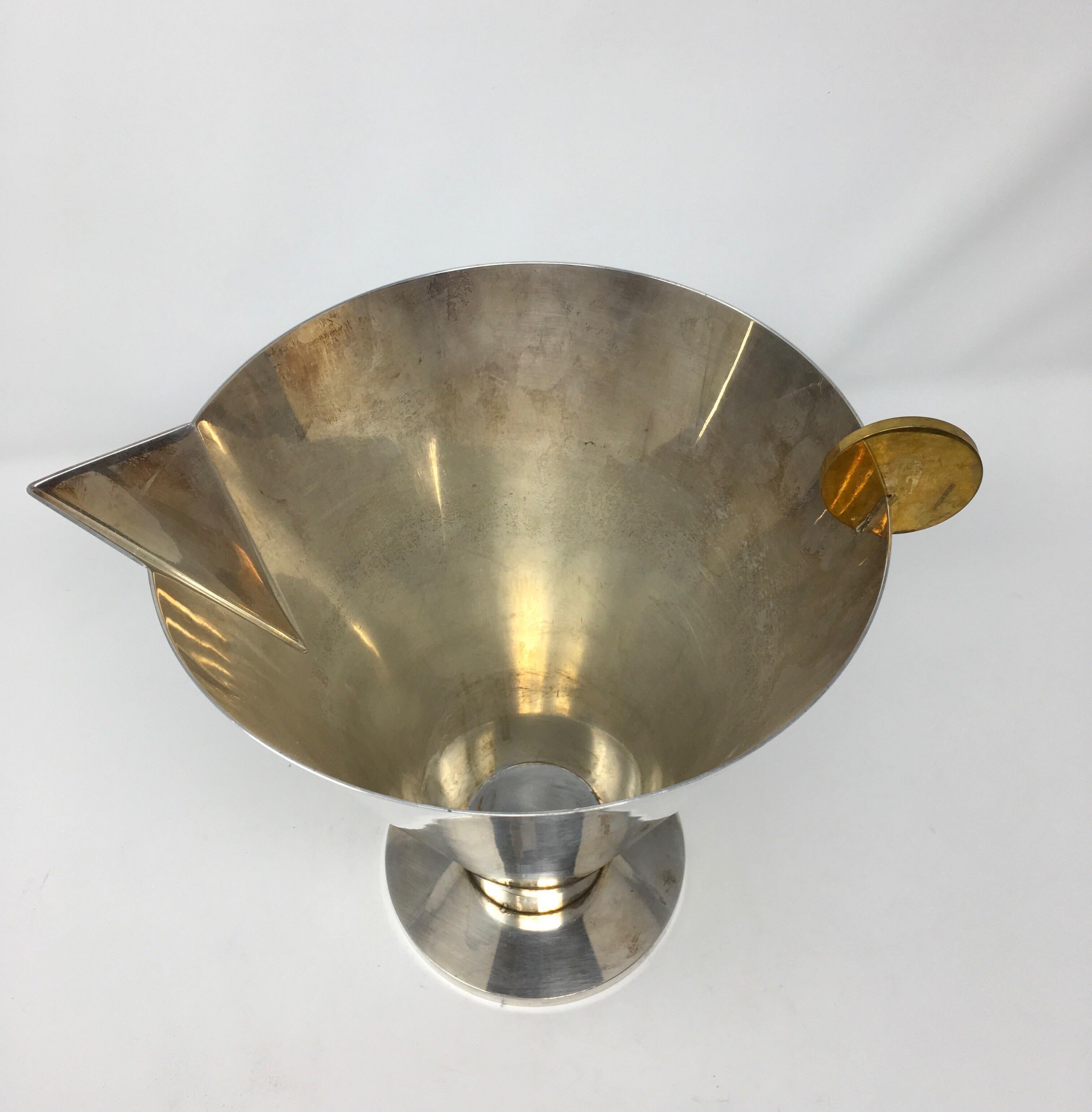 This is a Mid-Century Modern cocktail pitcher designed by Ambrogio Pozzi. The pitcher is made of silver plate with a brass circle attached to the rim. Ambrogio Pozzi was born in Varese, Italy. In 1951 Pozzi started designing and designed this piece