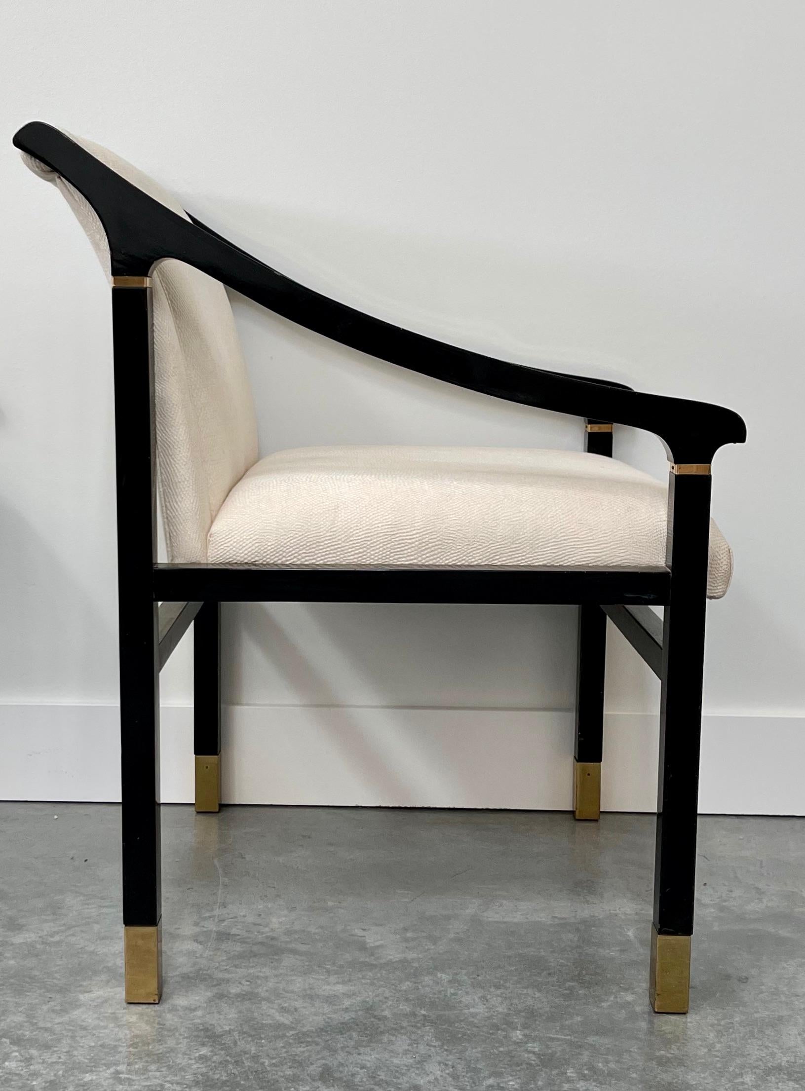 Hollywood Regency style dining chairs by Mastercraft. These sleek Mid-Century Modern sculptural arm chairs have unique sloped arm rests, curved back rests, original black lacquer wood H-frames with gold/brass metal trim and brass metal inlaid