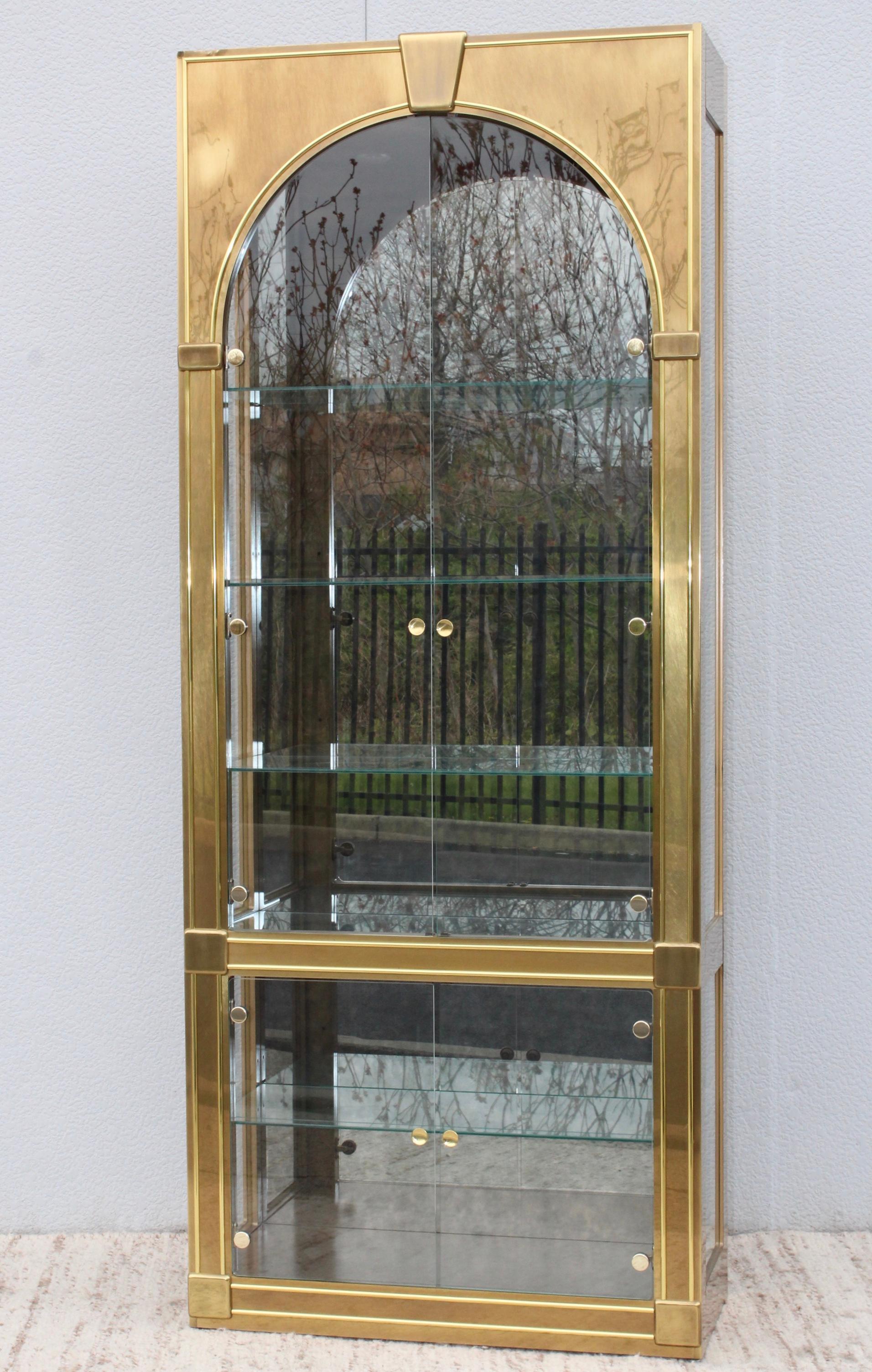 Stunning 1970s Mastercraft brass vitrine with glass shelves and antique mirror inside. In vintage original condition, there is s dent and wear on the upper left side.
