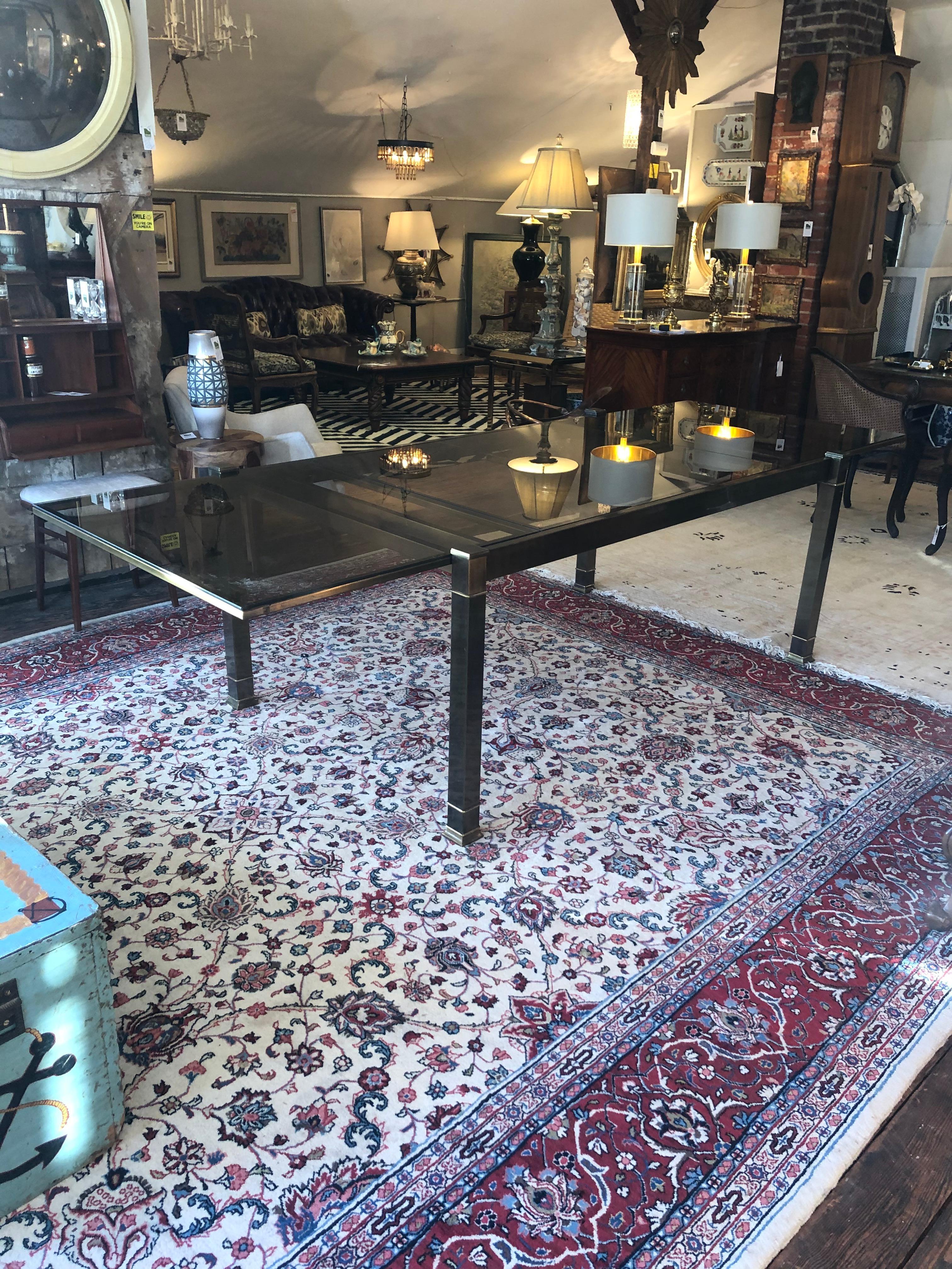 Ingeniously engineered Mid-Century Modern brass and warmly tinted glass expandable dining table with sleek design attributed to Mastercraft. Each end easily pulls out to open the central space where a central leaf raises up easily via an internal