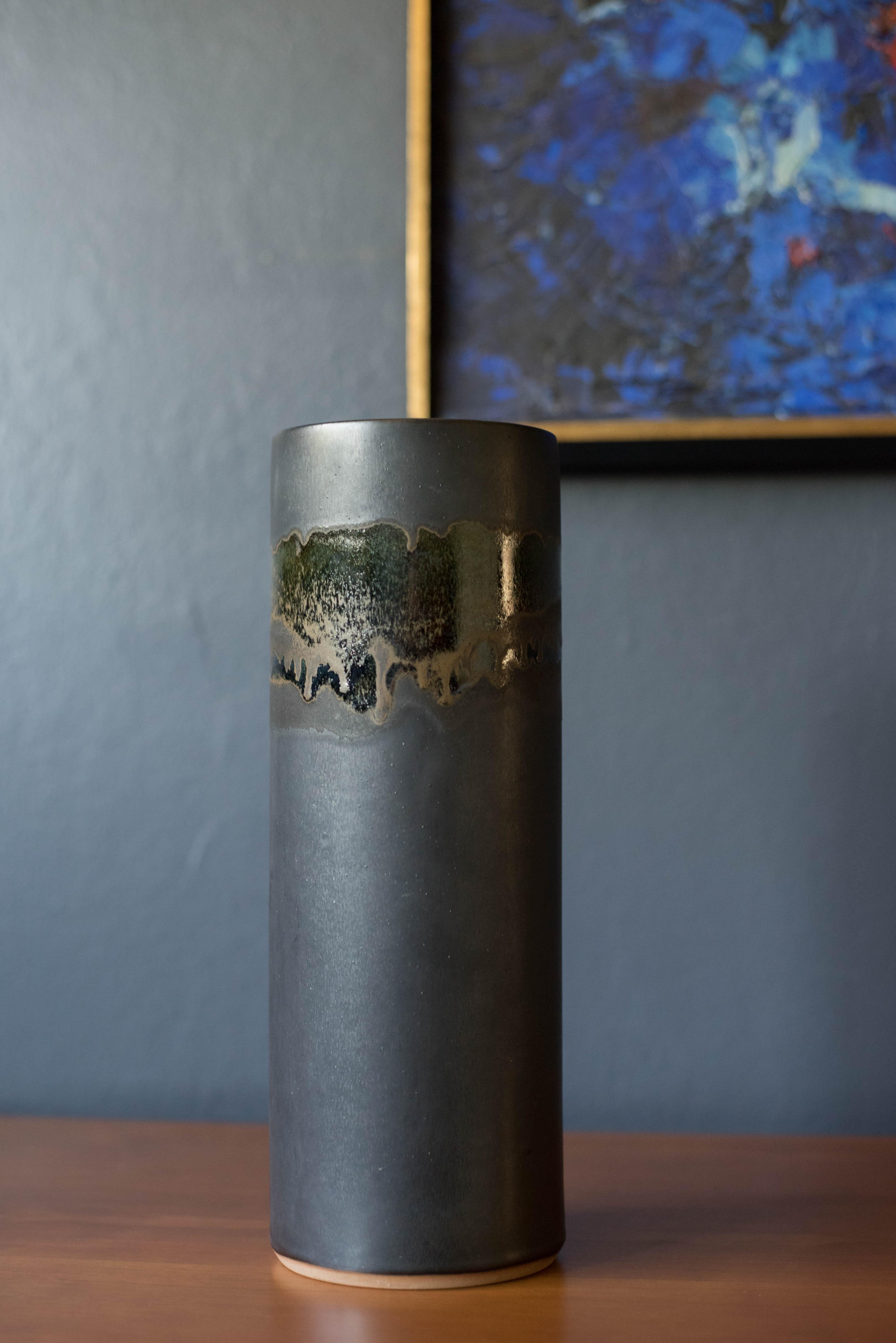 Vintage stoneware studio pottery cylinder vase circa 1960's. This decorative piece features a dark matte blue finish with a crystalline drip glaze in shades of black, brown, and green. Engraved 'A' on the underside of vessel. 

 