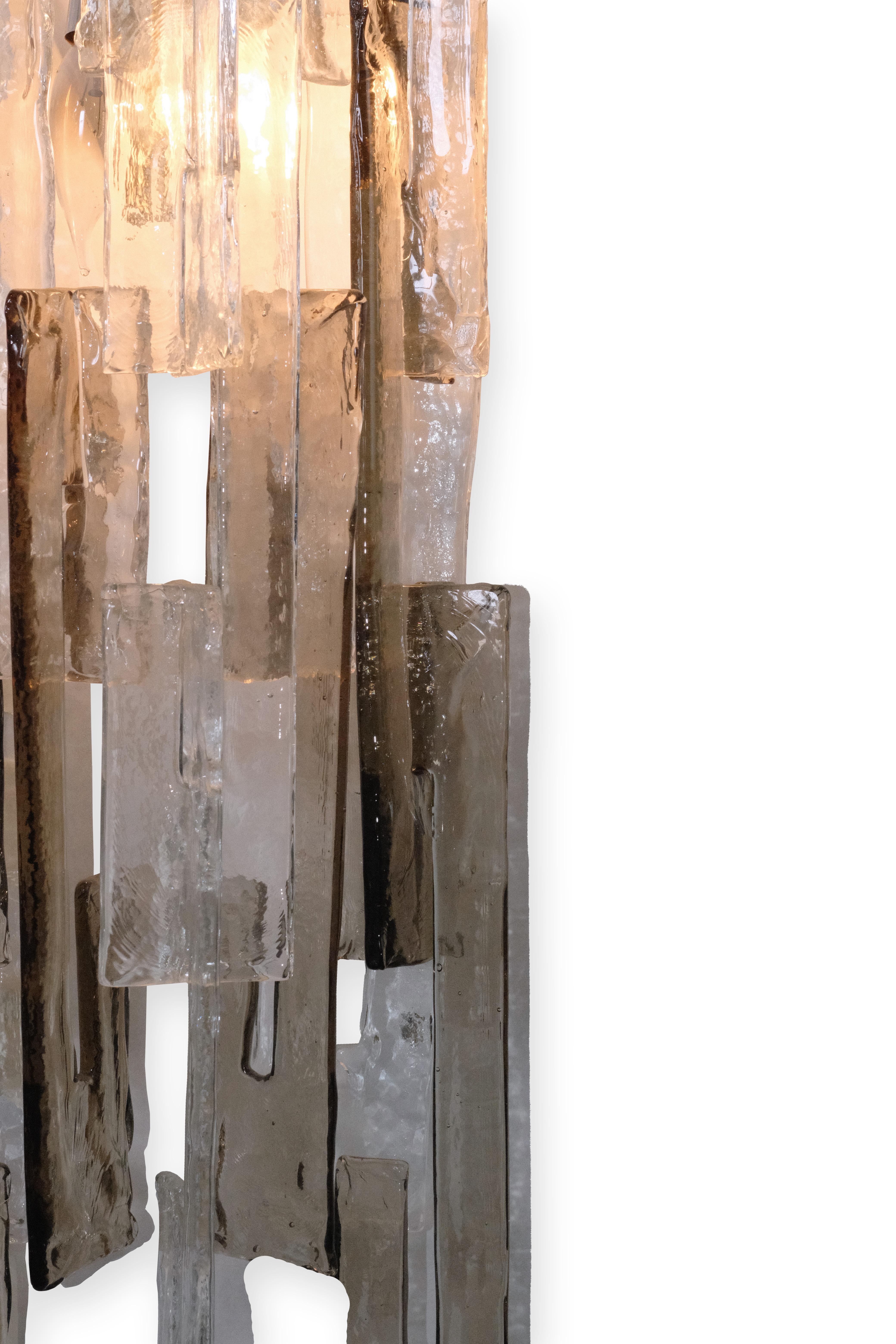 A striking and singular pair of large Murano glass sconces by Mazzega. Handcrafted from clear and smoke-gray Murano glass, each interlocking element—gracefully shaped like the letter 'C'—fits together in a sculptural dance of light and form.

Place