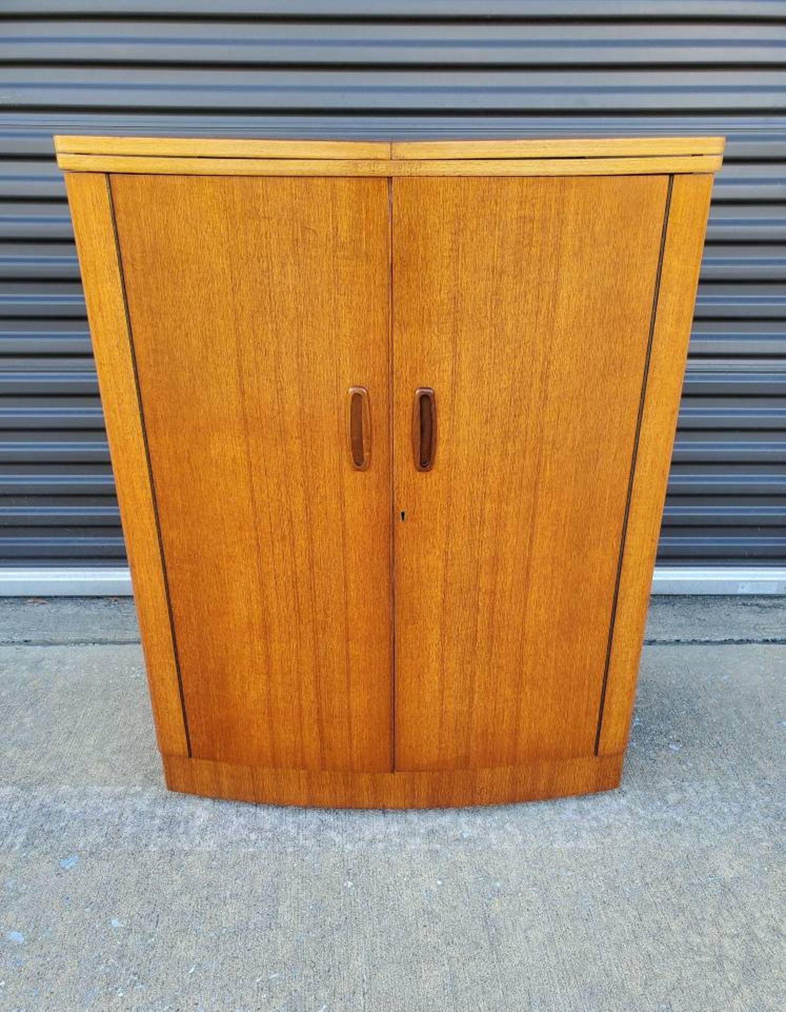 A fabulous British Danish designed Mid-Century Modern teak liquor cabinet dry bar by Turnidge of London. Circa 1960

This signed, highly coveted morphing cocktail cabinet is a gorgeous space saving design that opens, two tone, the top unfolds and