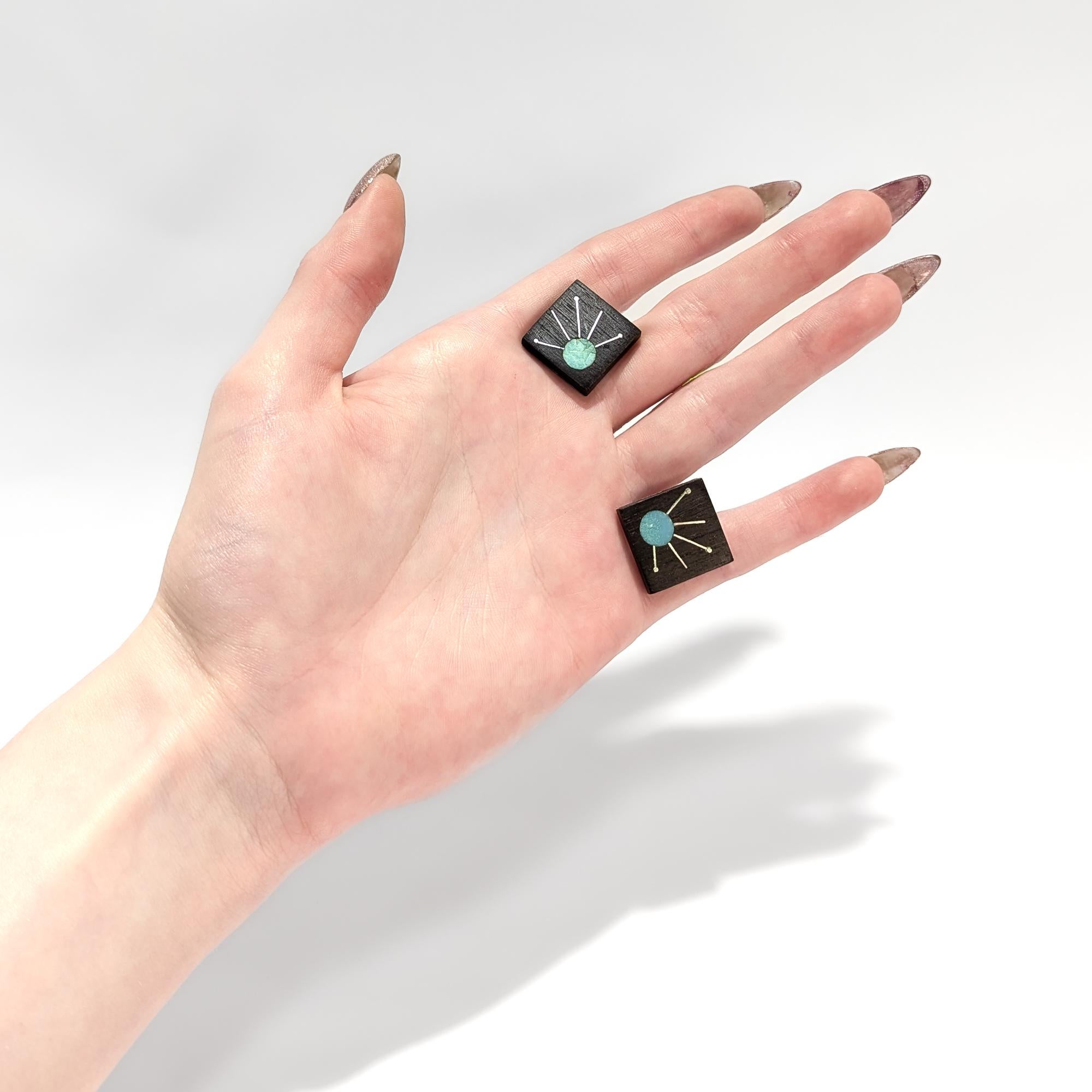 Un fino par de gemelos modernistas mexicanos.

En plata de ley.

Con una incrustación de madera oscura. 

Con caras cuadradas, cada una de ellas con un círculo incrustado de piedra dura (probablemente amazonita) del que salen rayos de plata que